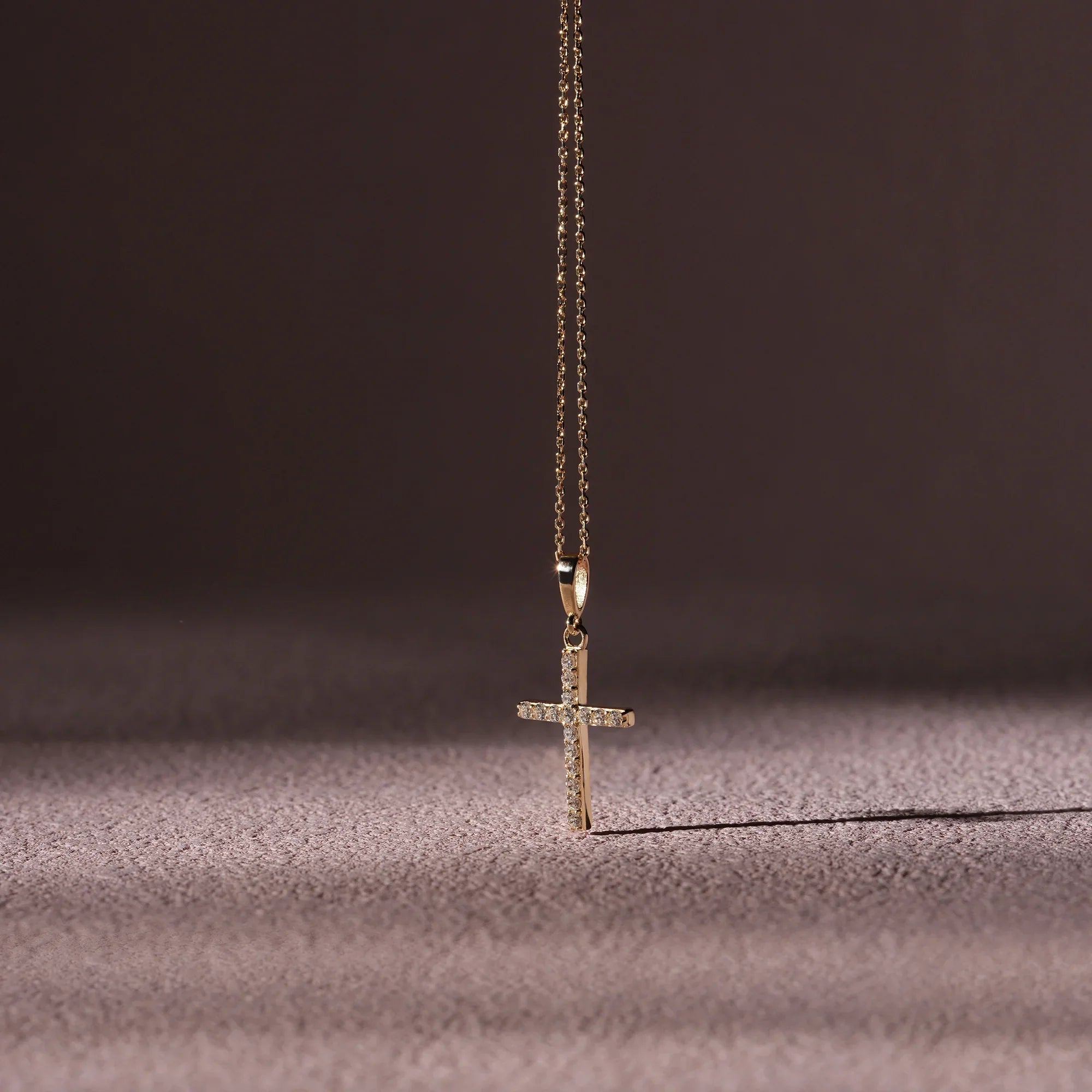 Gold cross necklace on a textured surface with a dark background