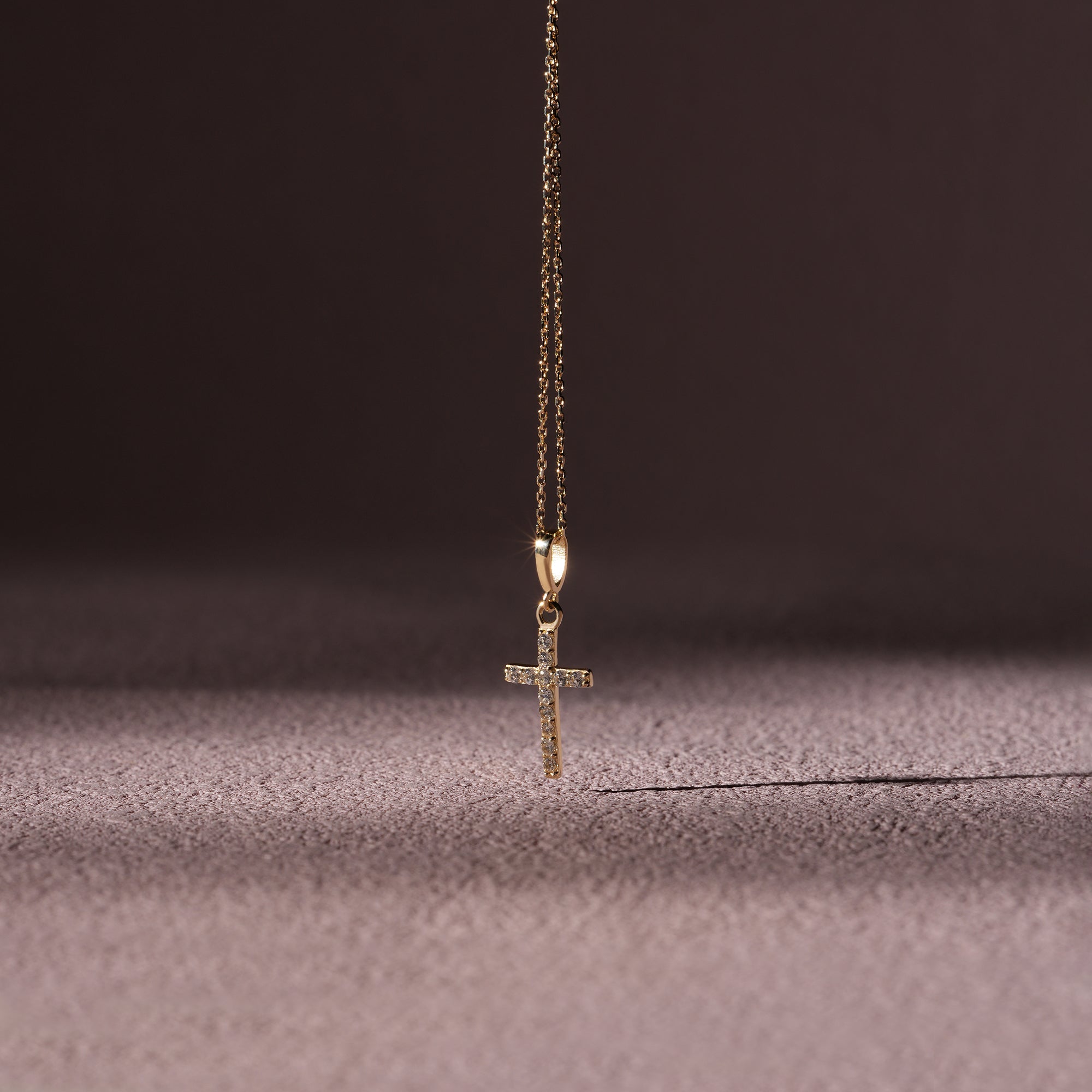 Gold cross necklace on a textured surface with a dark background