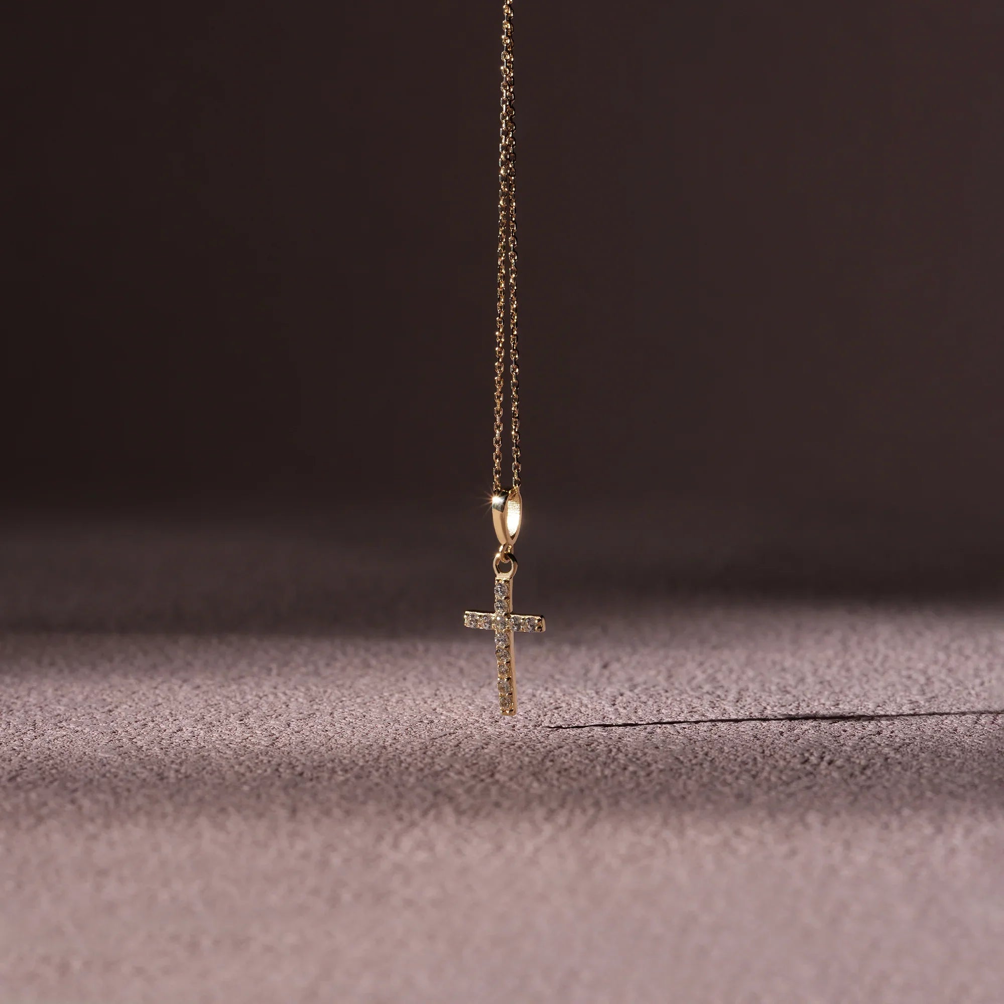 Gold cross necklace on a textured surface with a dark background