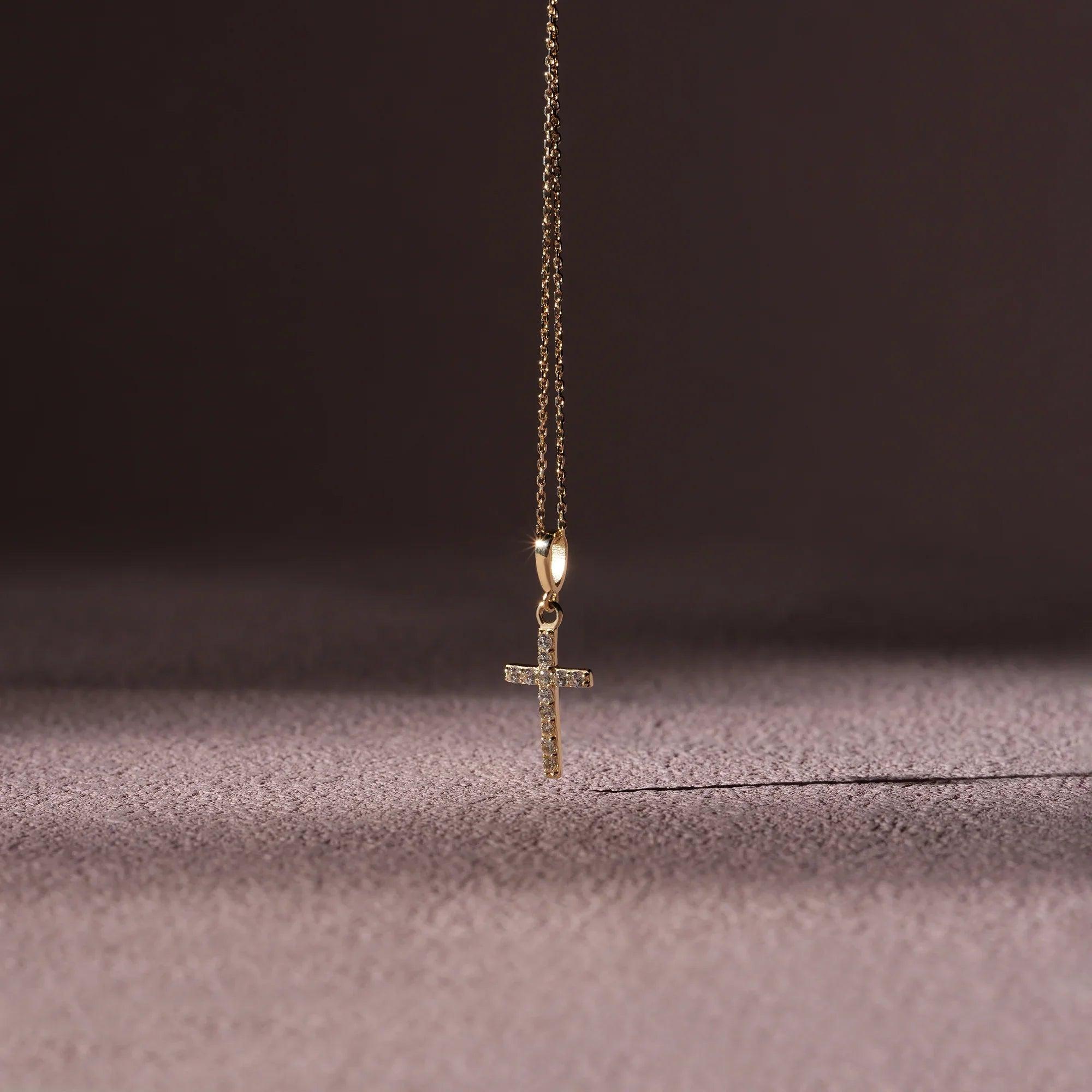 Gold cross pendant necklace with small diamonds on a soft textured surface