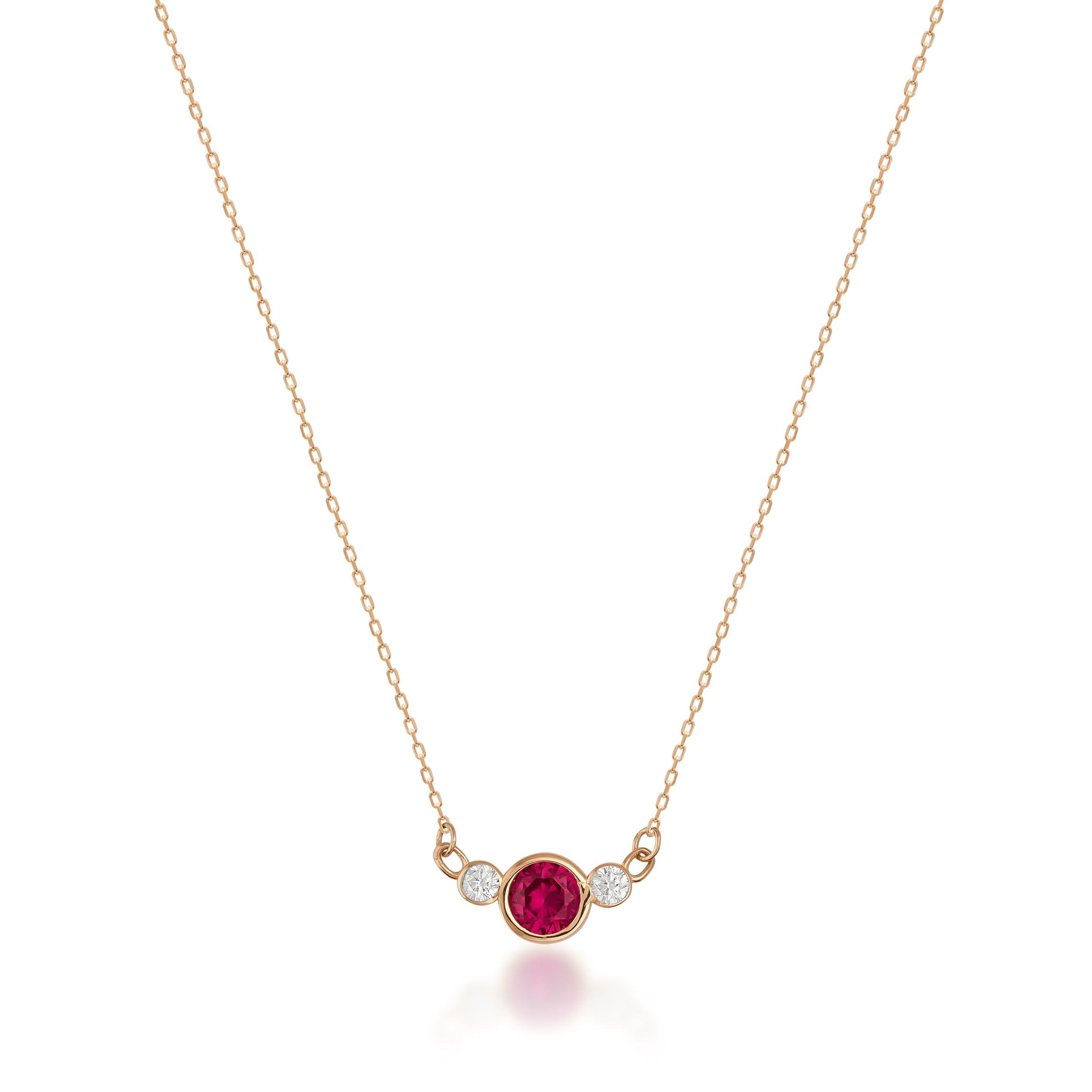Gold necklace with a round red gemstone and two small diamonds on a delicate chain