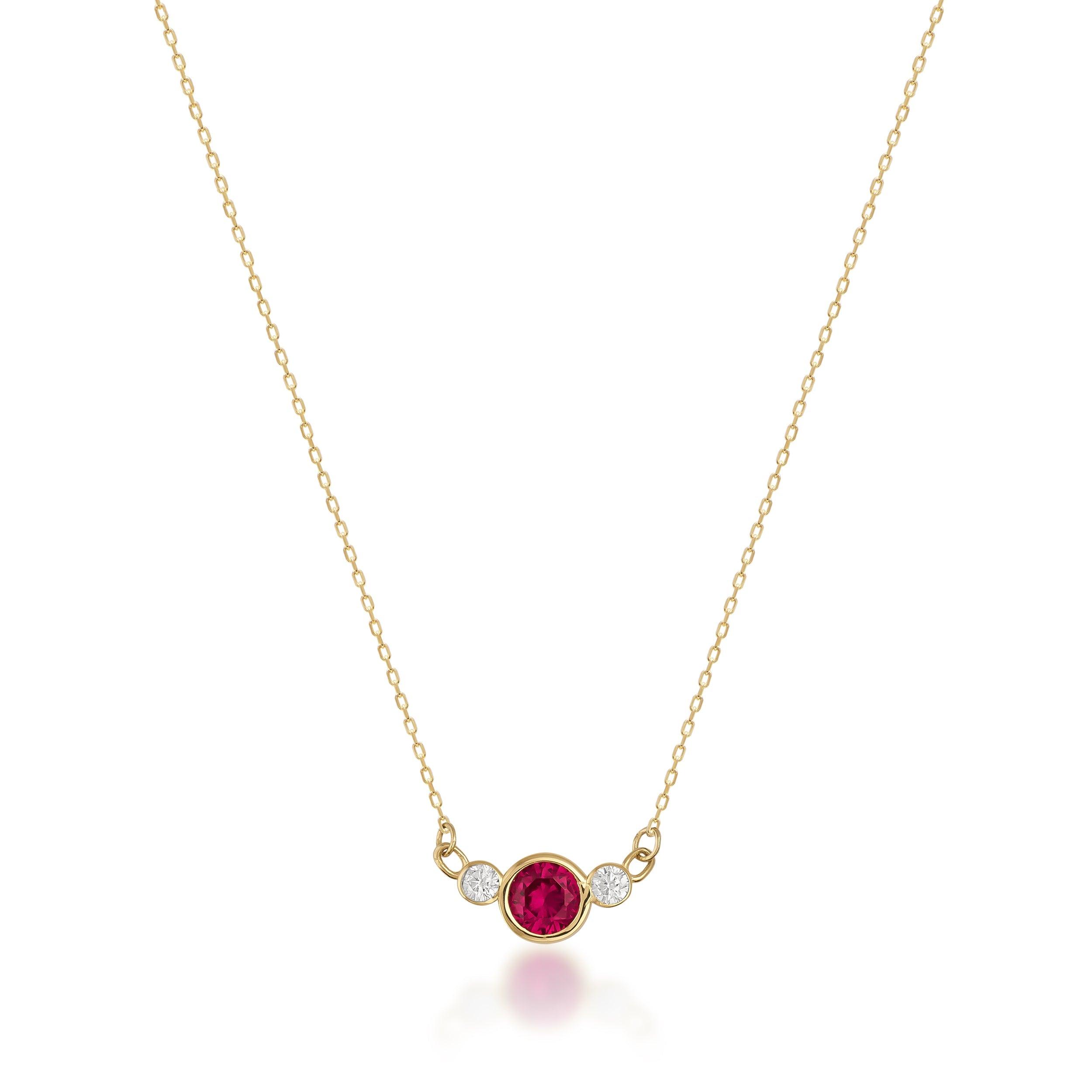 Gold necklace with central red gemstone and two small clear stones on white background