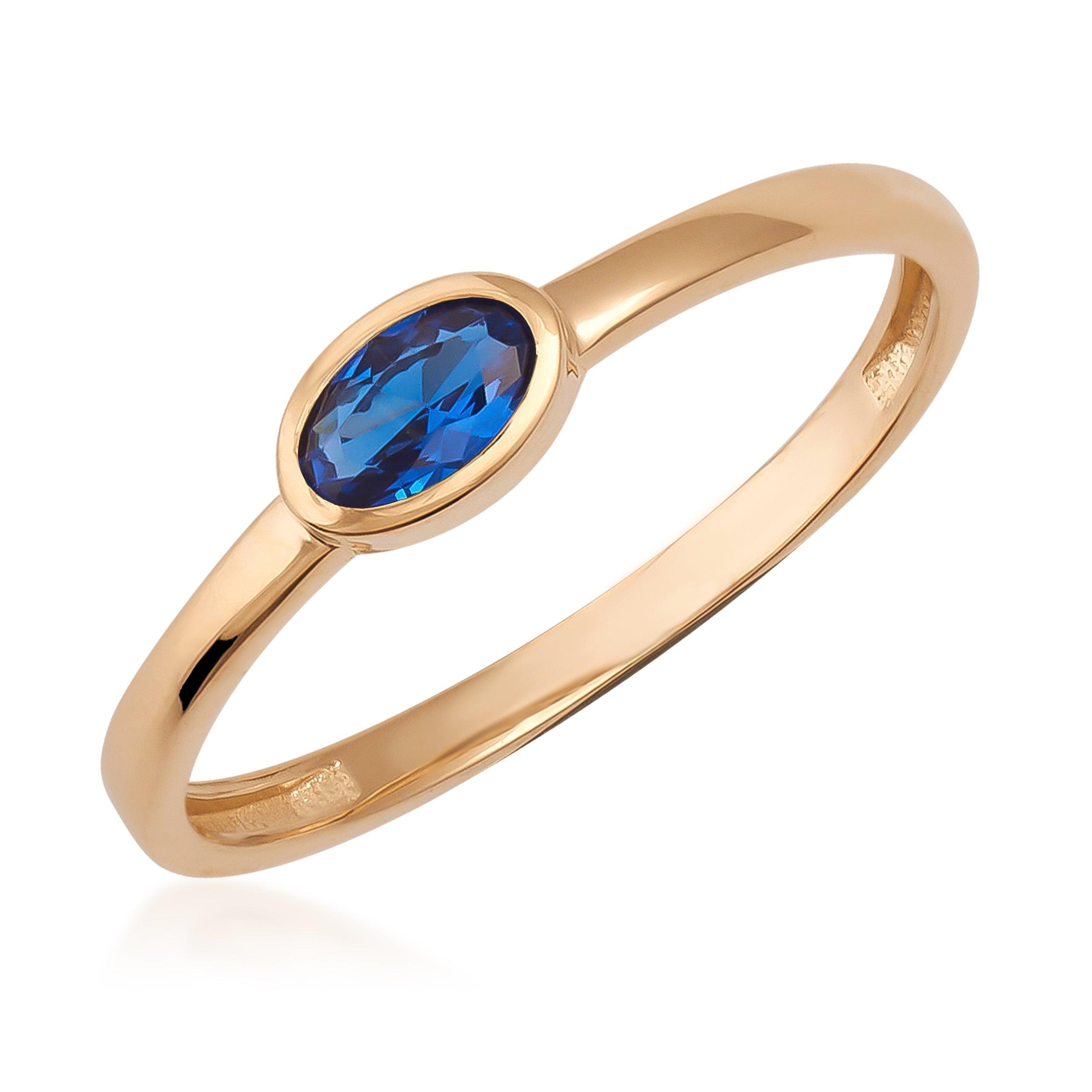 Gold ring with an oval blue gemstone in a simple bezel setting on white background