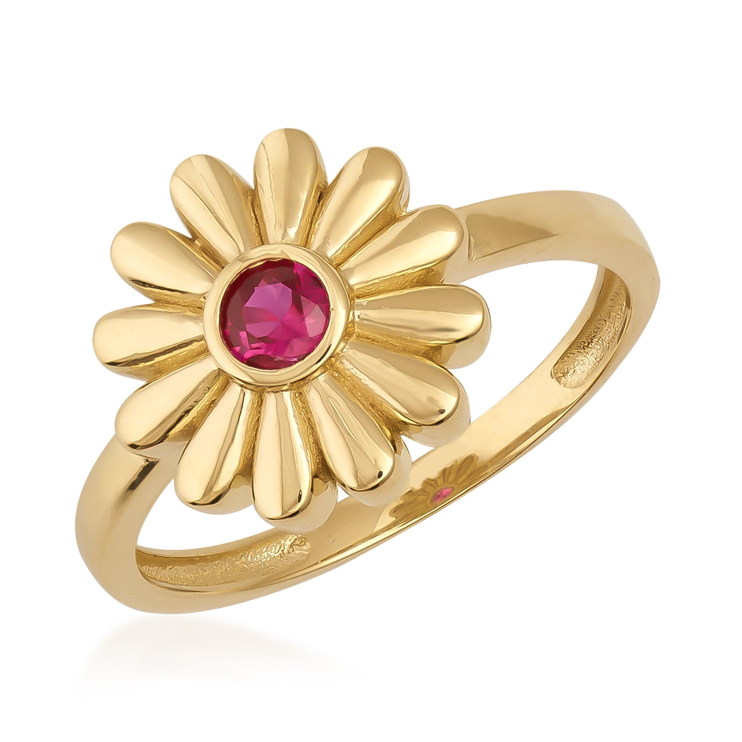 Gold daisy flower ring with a round red gemstone center on a white background