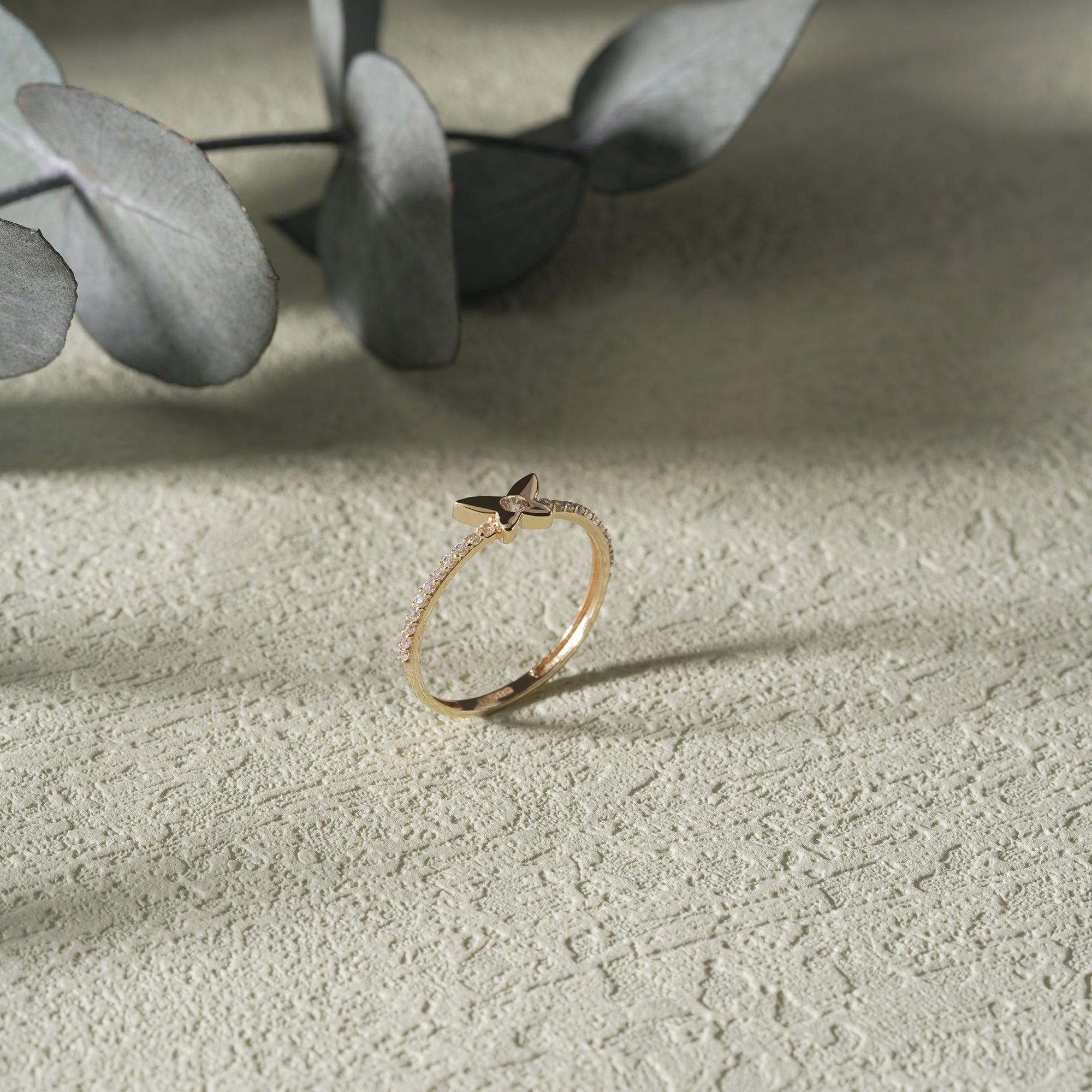 Delicate gold ring with butterfly design and small accent stones on textured surface.