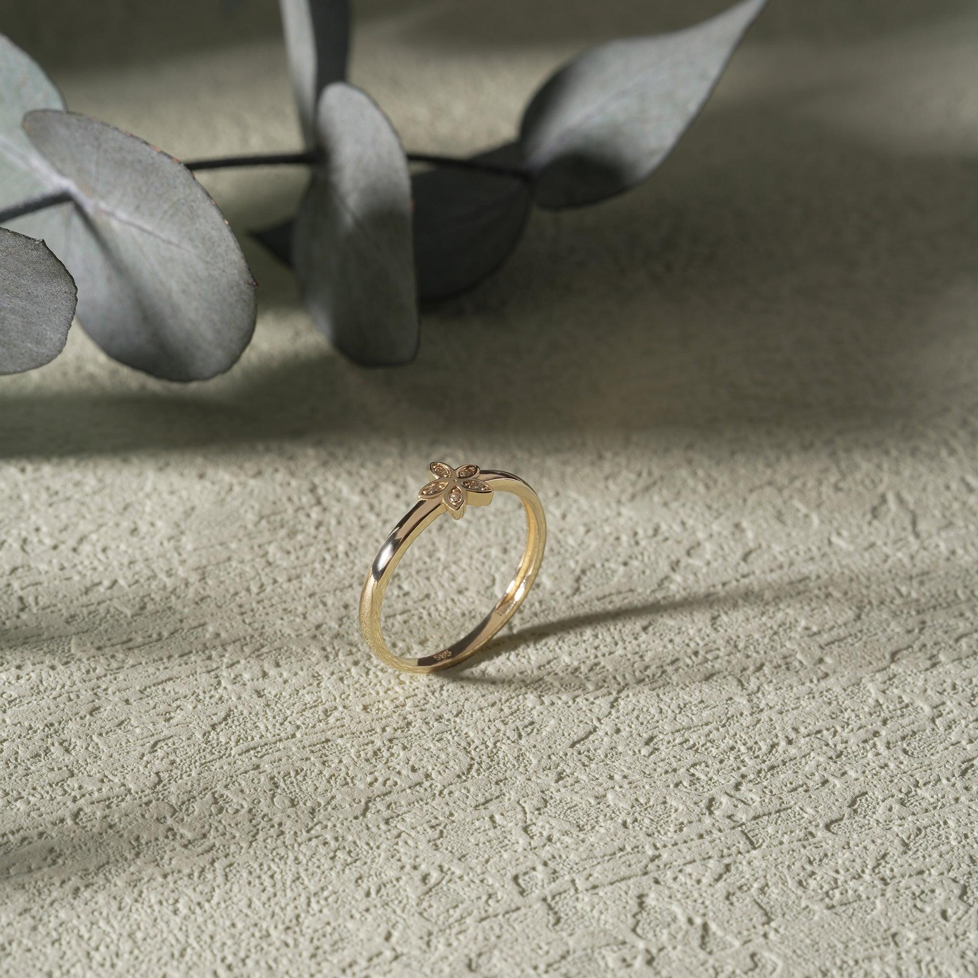 Delicate gold ring with small floral design on textured surface, elegant jewelry closeup