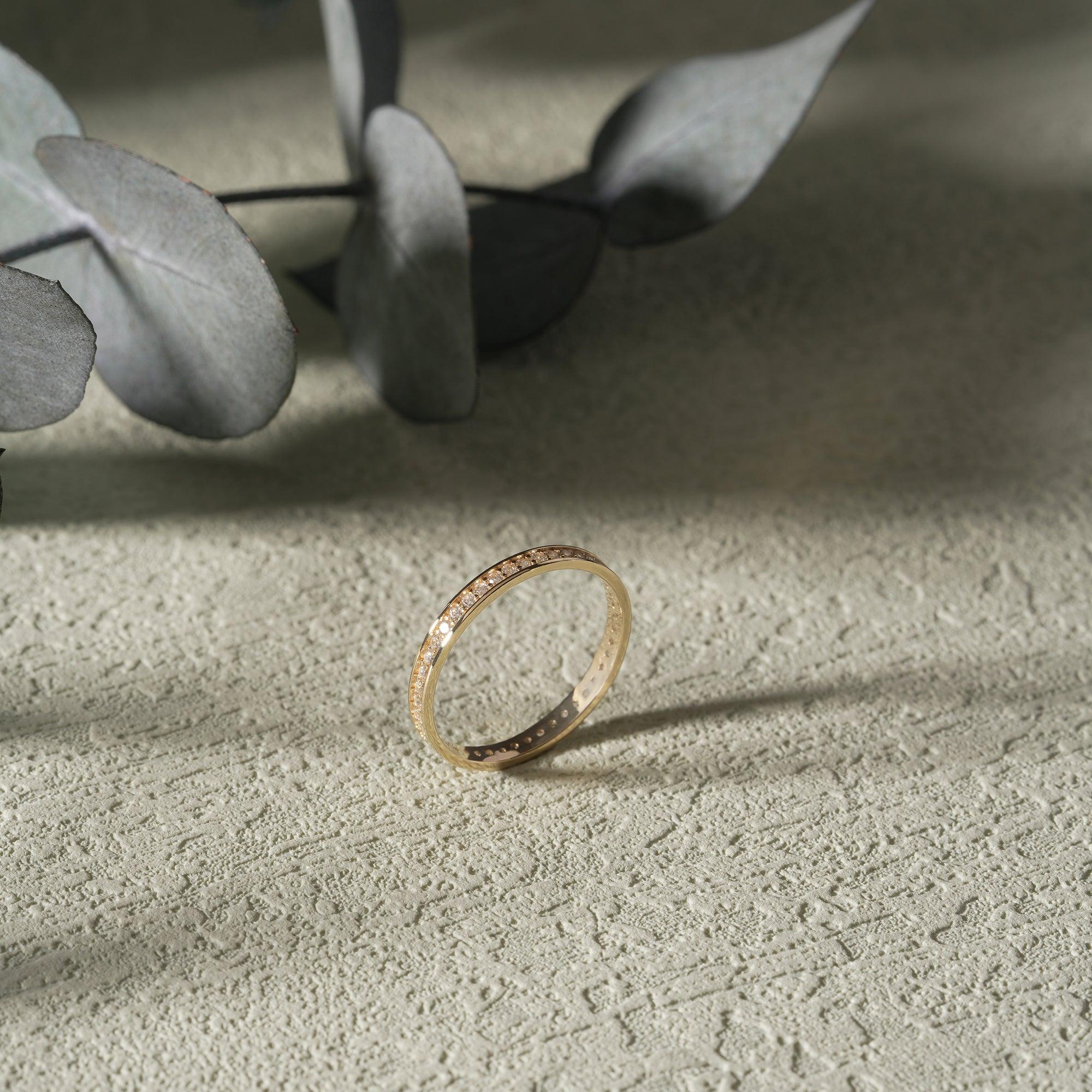 Gold diamond band ring on textured surface with eucalyptus leaves in soft sunlight