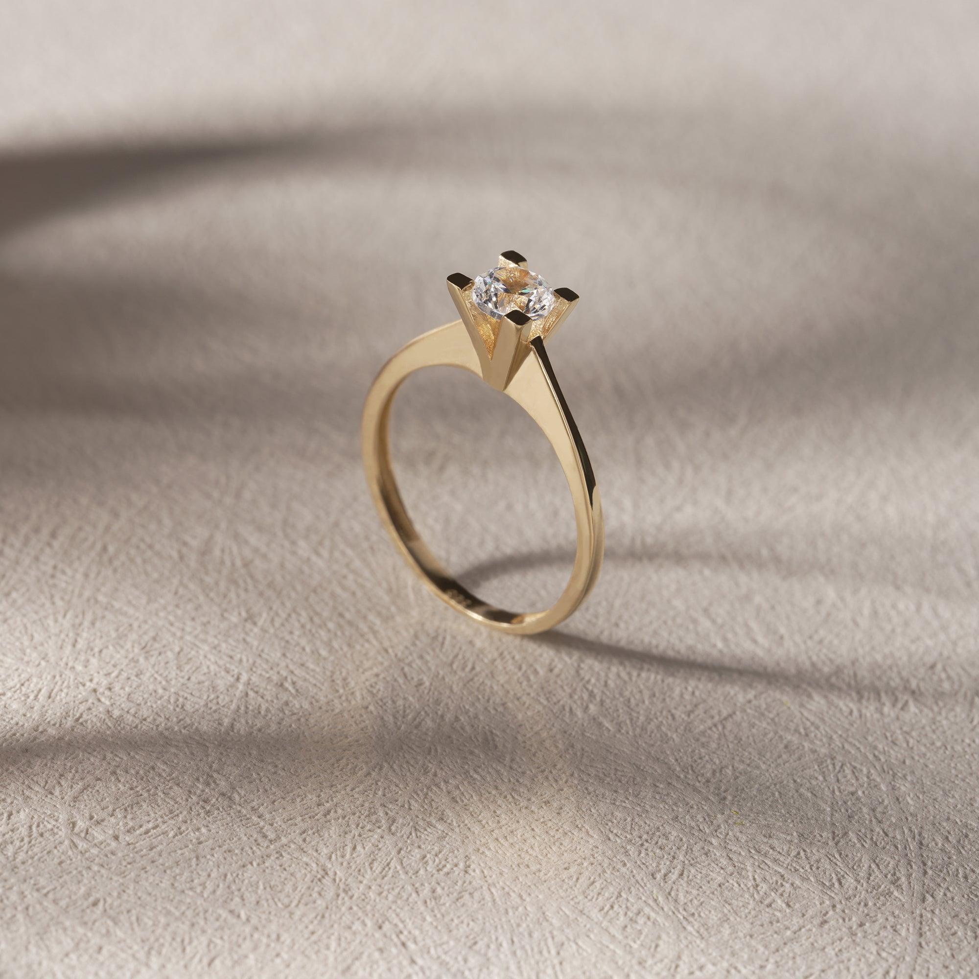 Gold solitaire engagement ring with round diamond on textured beige surface