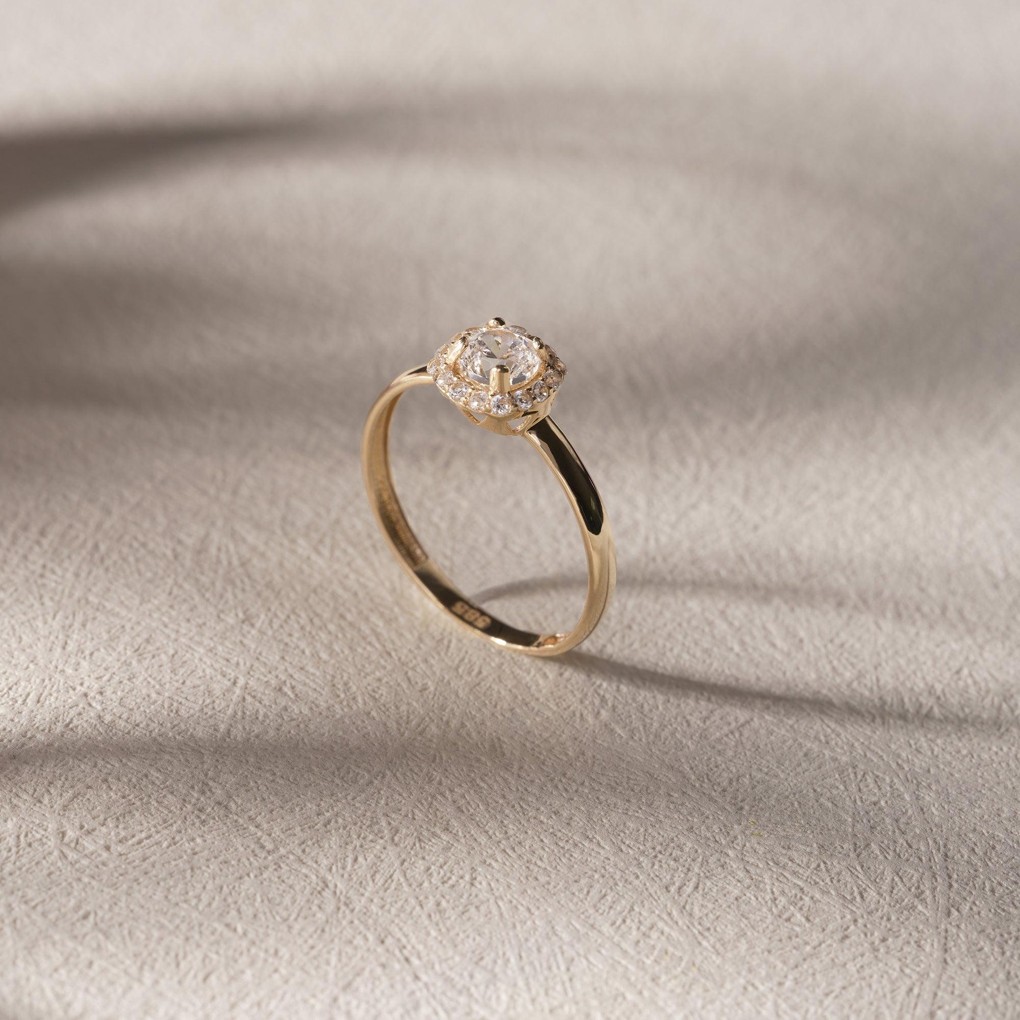 Elegant gold engagement ring with oval-cut center stone and diamond halo on textured surface