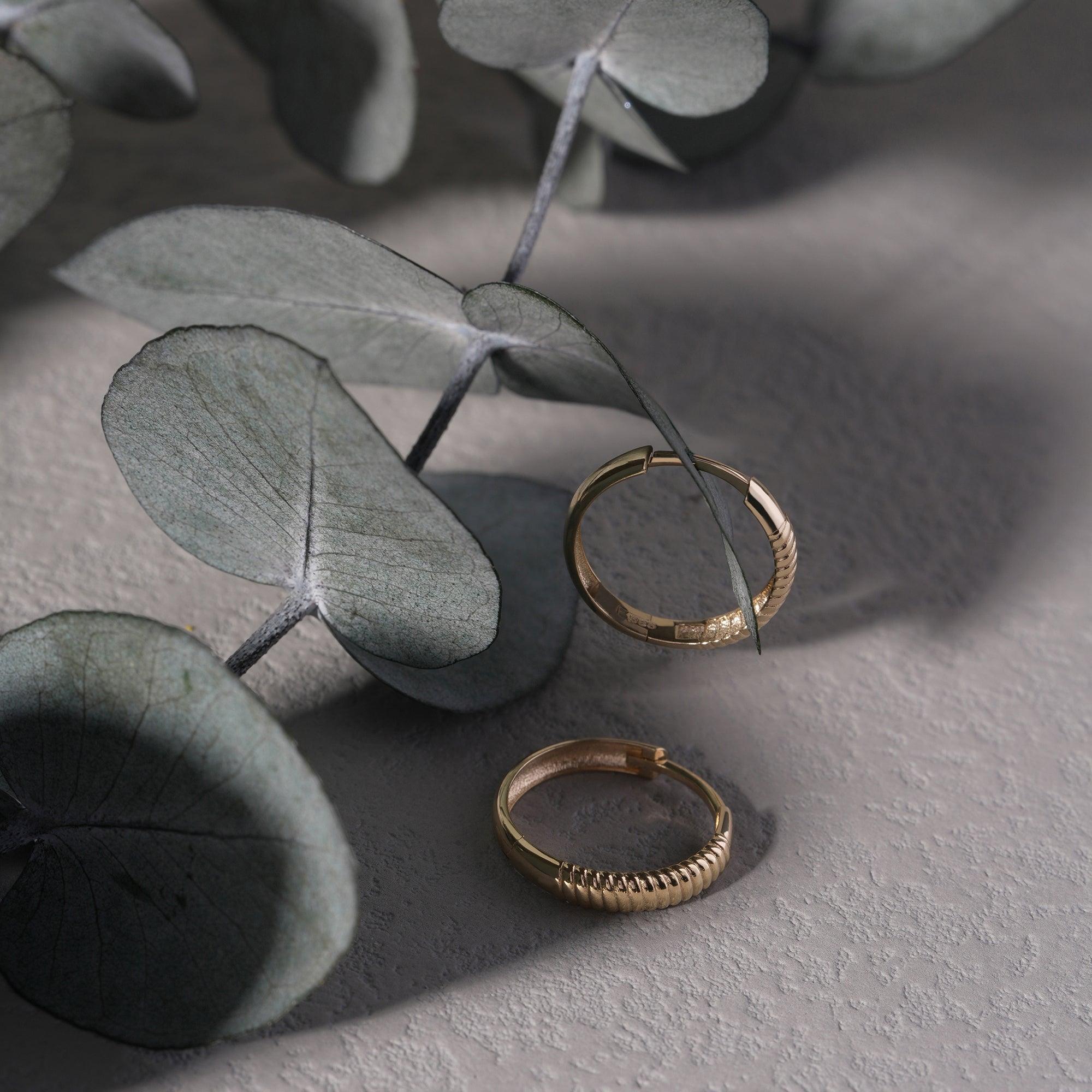 Gold hoop earrings with textured design on a gray textured surface and eucalyptus leaves