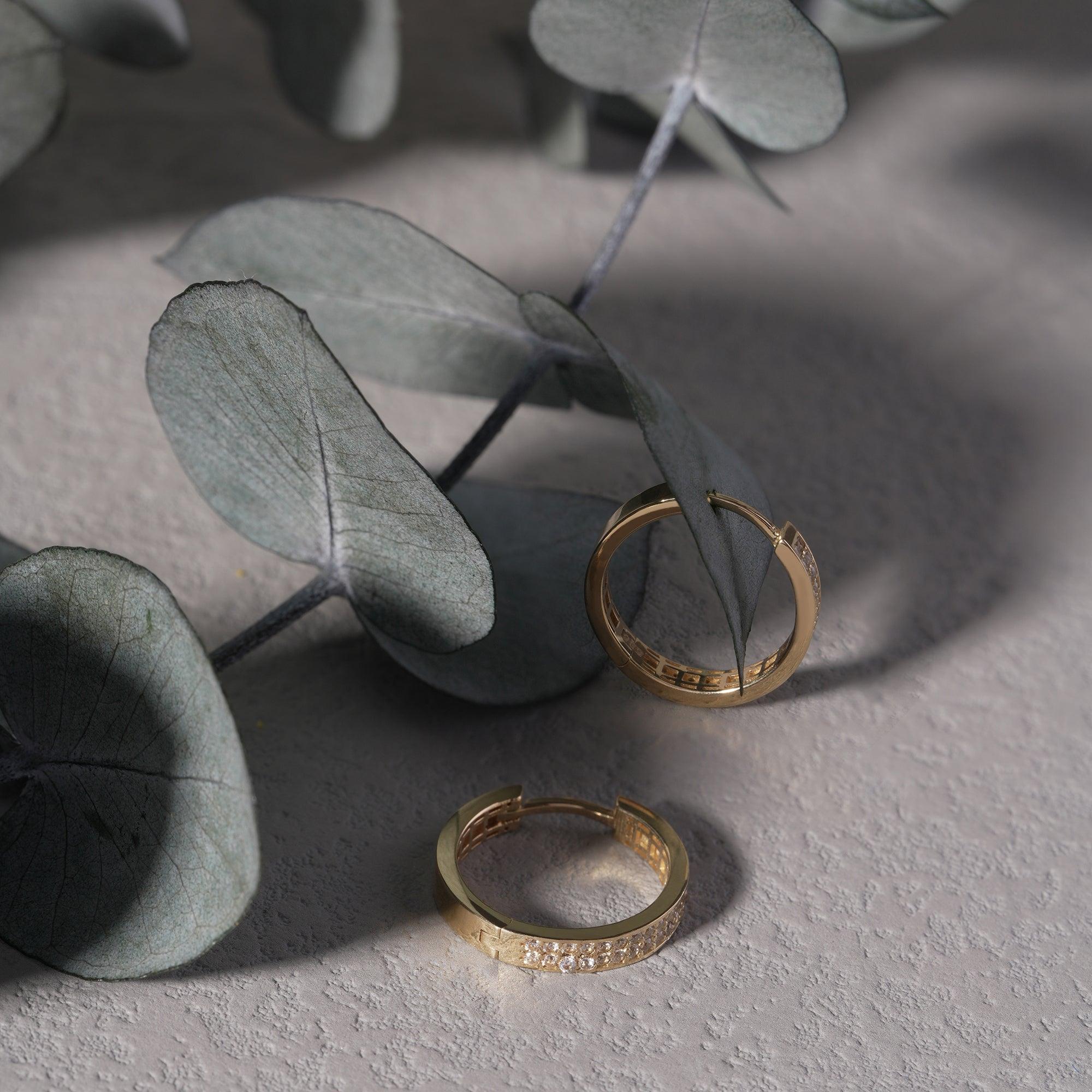 Gold hoop earrings with small diamonds on textured surface and eucalyptus leaves