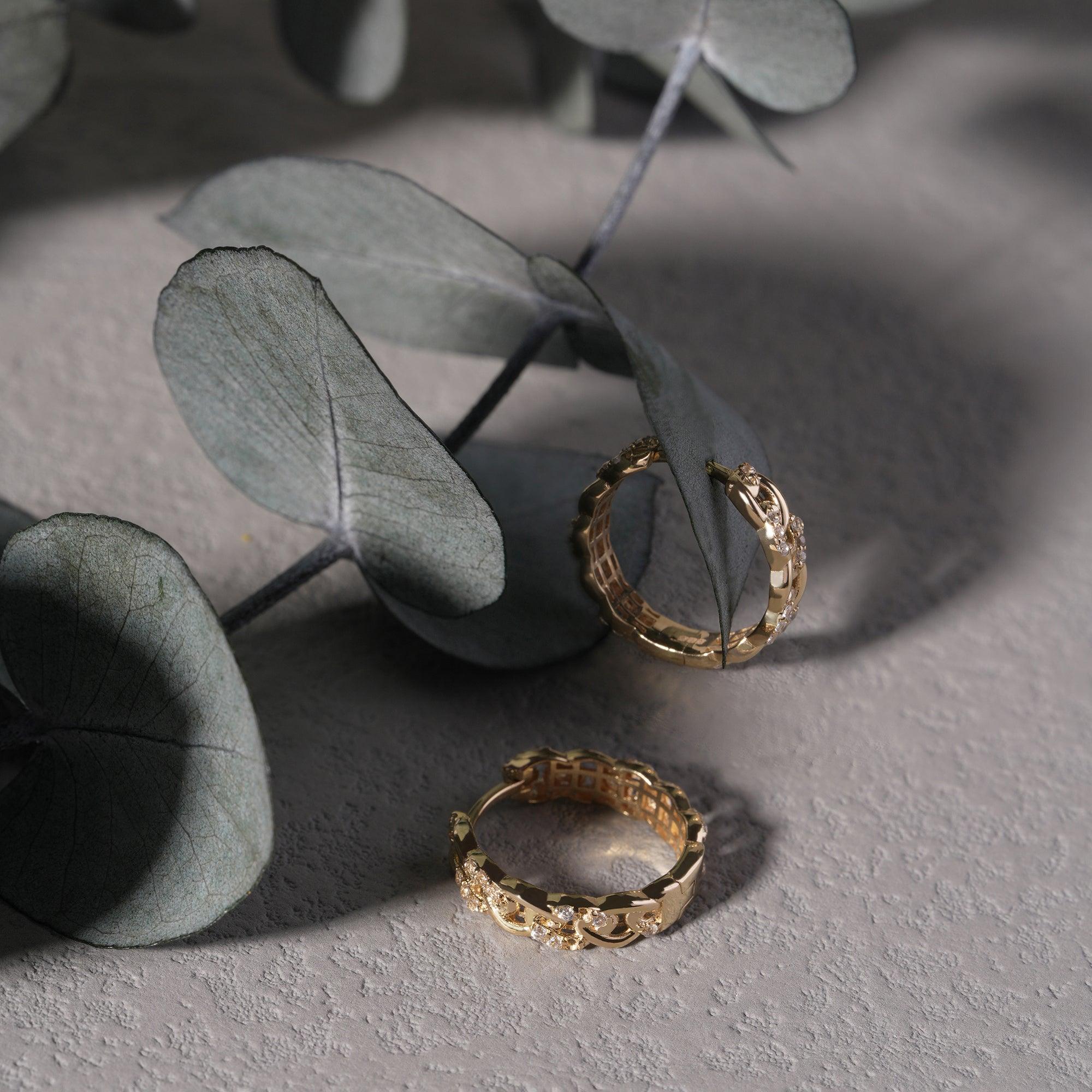 Gold hoop earrings with floral detailing on textured surface and eucalyptus leaves