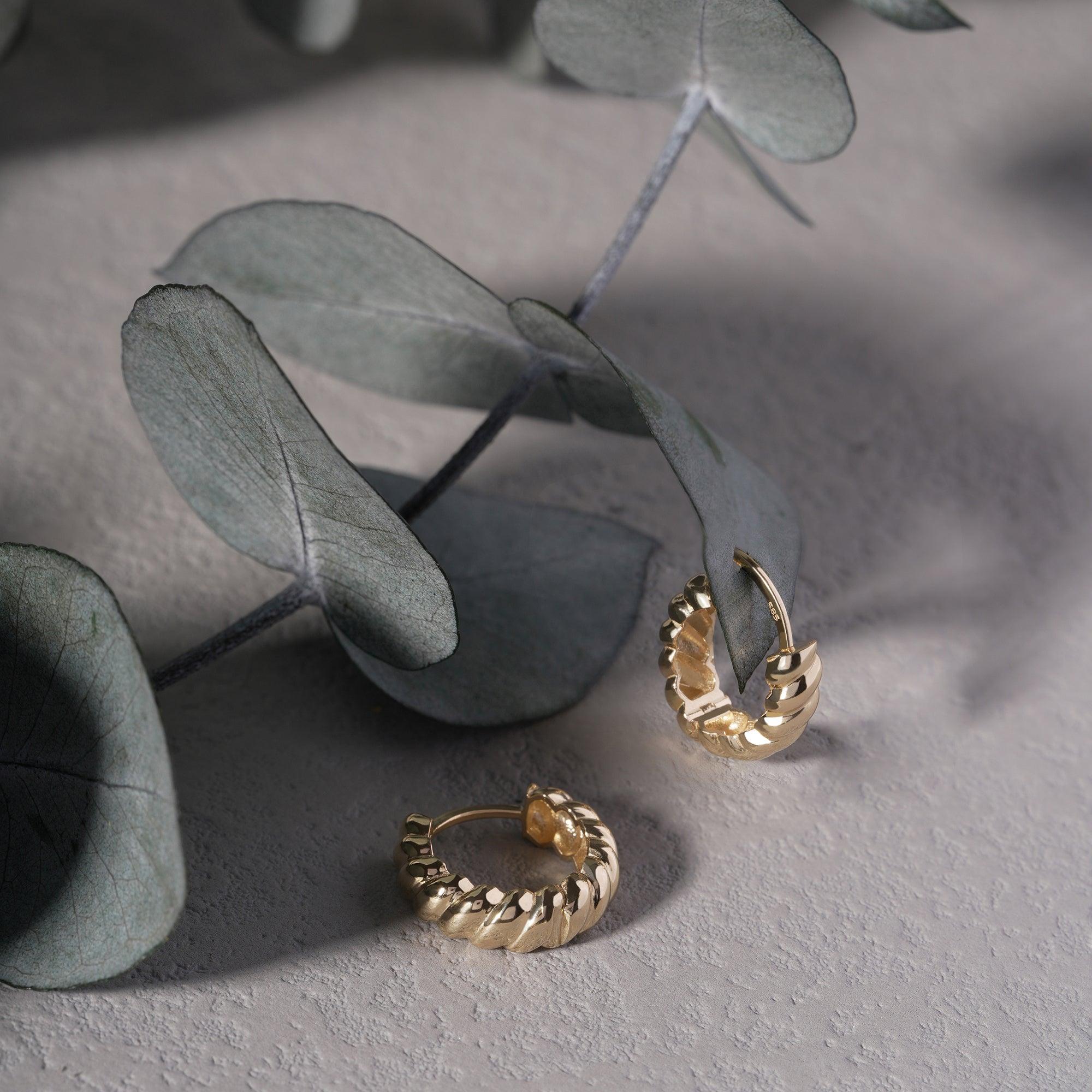 Textured gold hoop earrings on a gray surface with eucalyptus leaves