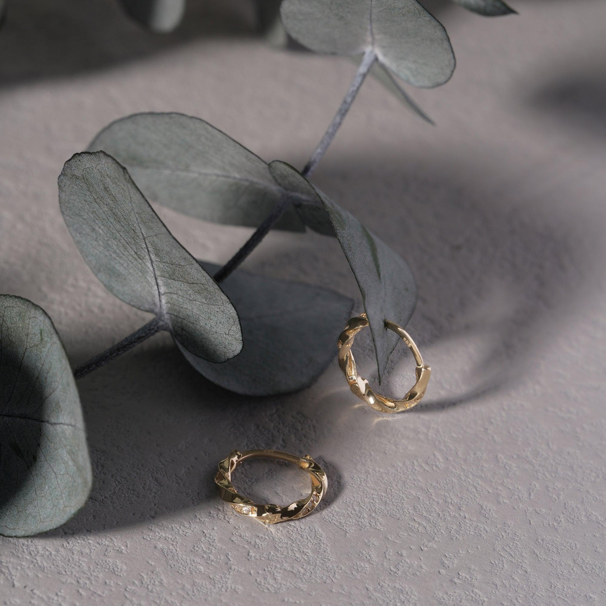 Textured gold hoop earrings on light stone surface with eucalyptus leaves