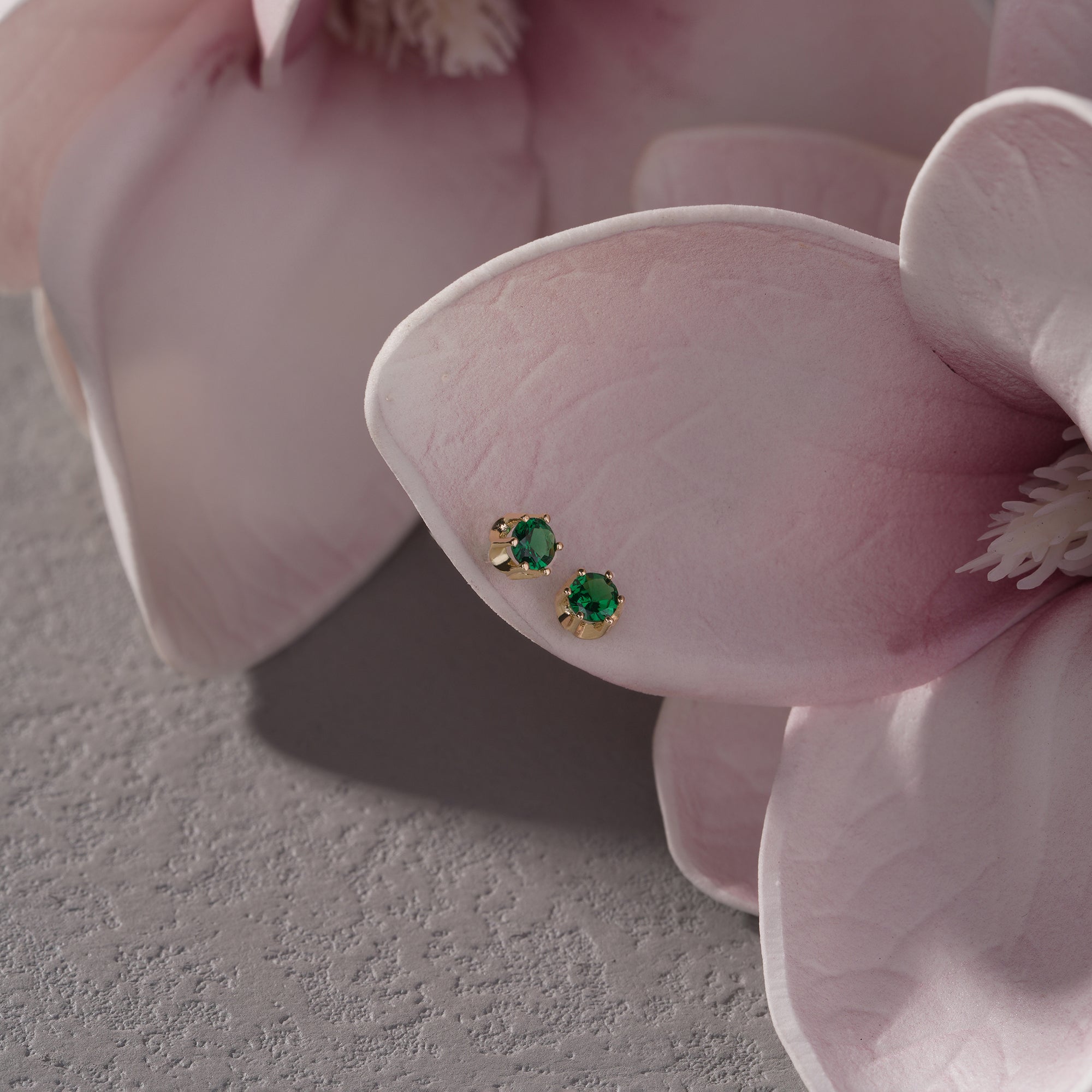 Pair of emerald green gemstone earrings on a pink orchid.