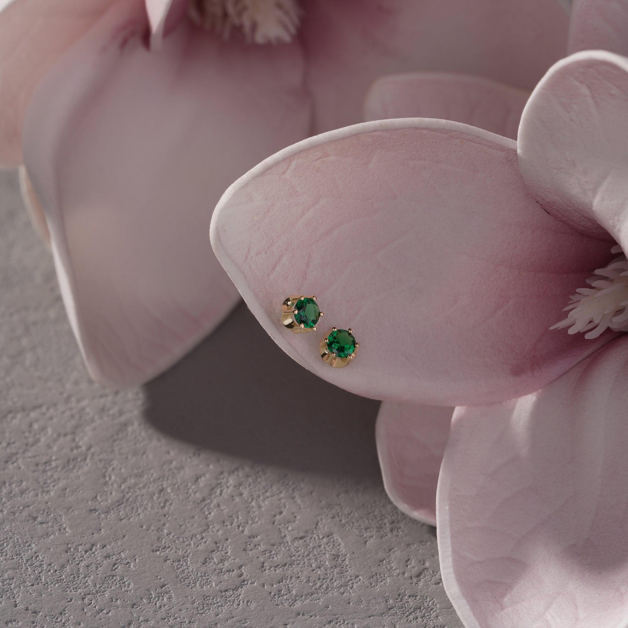 Gold stud earrings with green gemstones on pink flower petals, elegant jewelry closeup