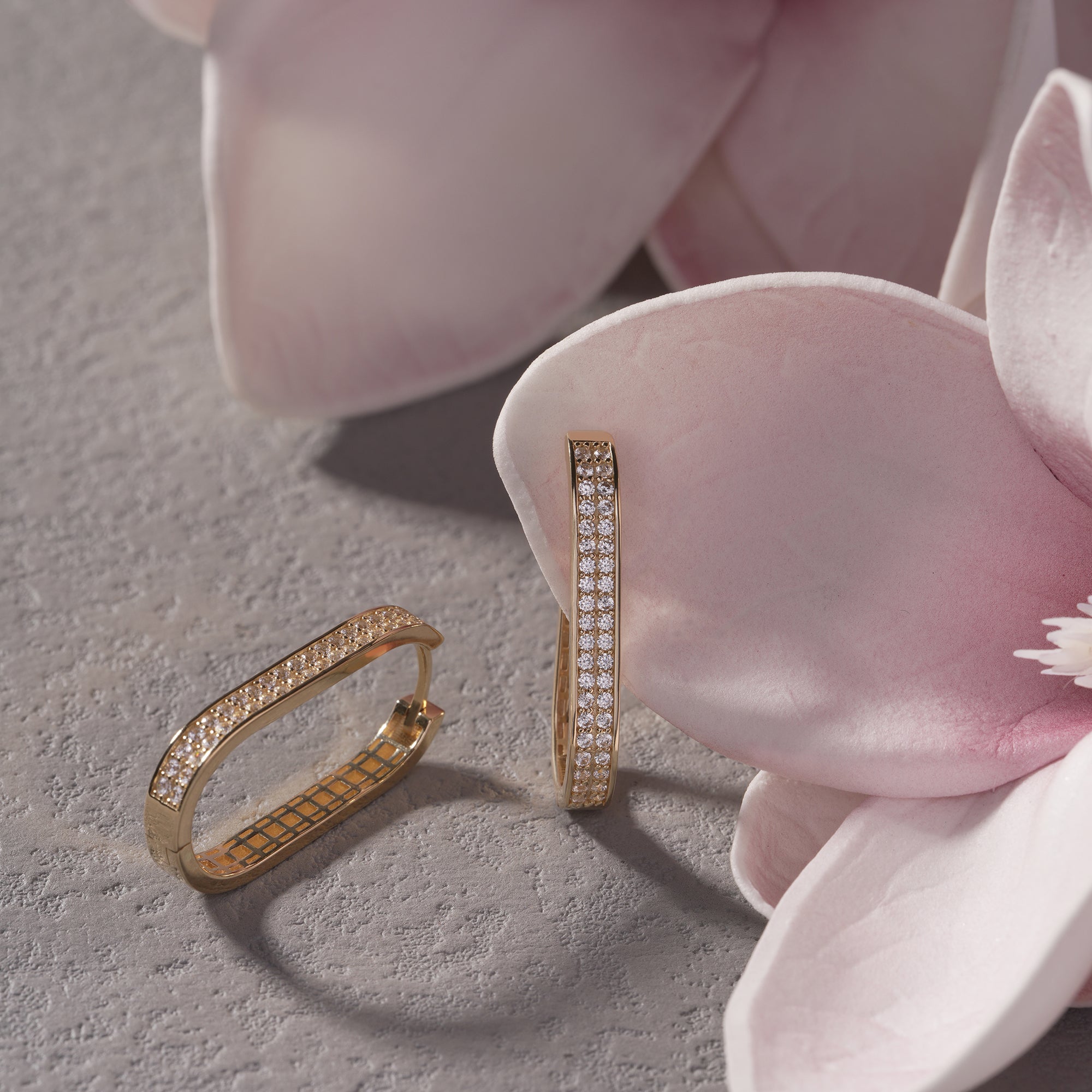 Gold hoop earrings with diamond accents on a pink flower petal.