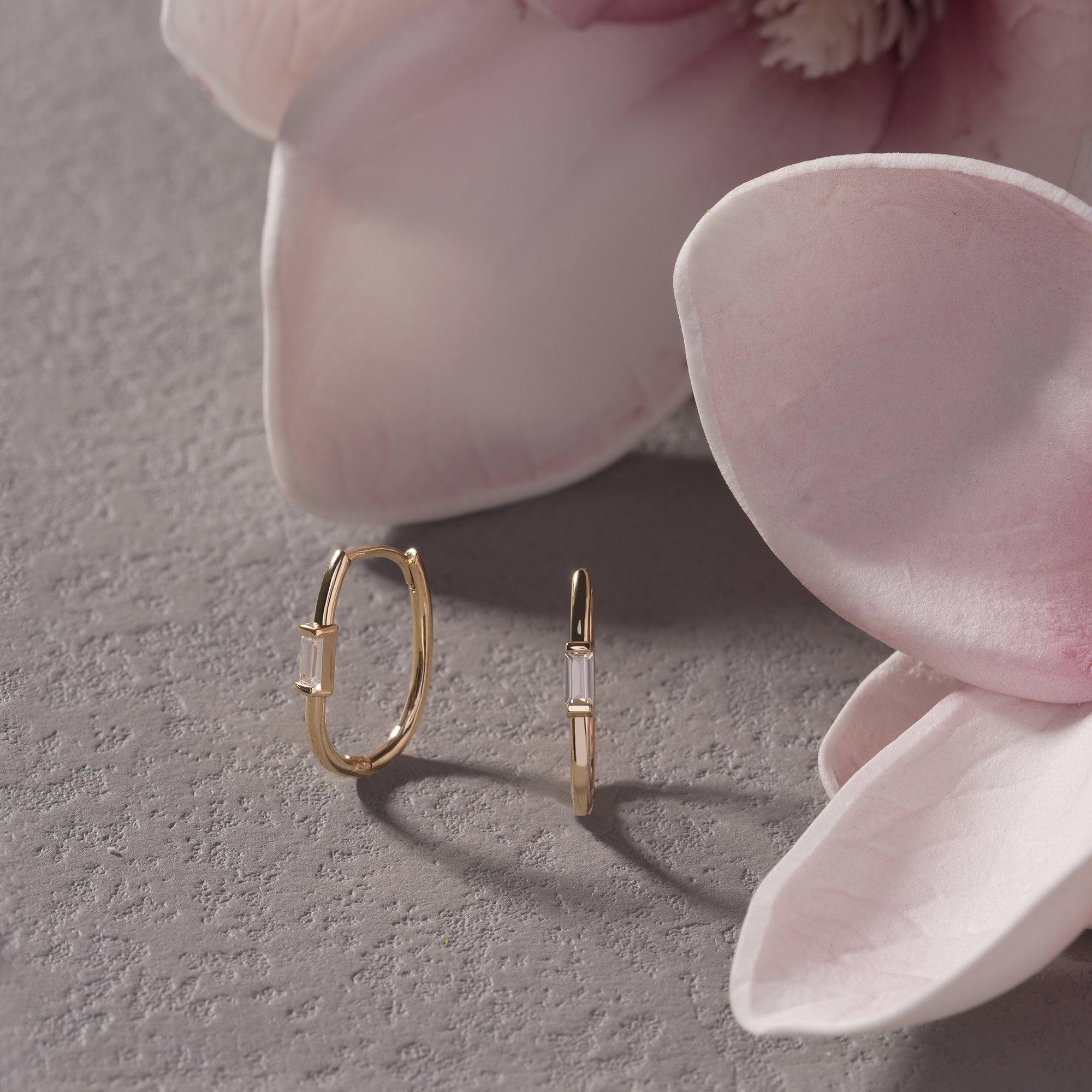Gold hoop earrings with baguette crystals on a textured surface, styled with pink flower petals