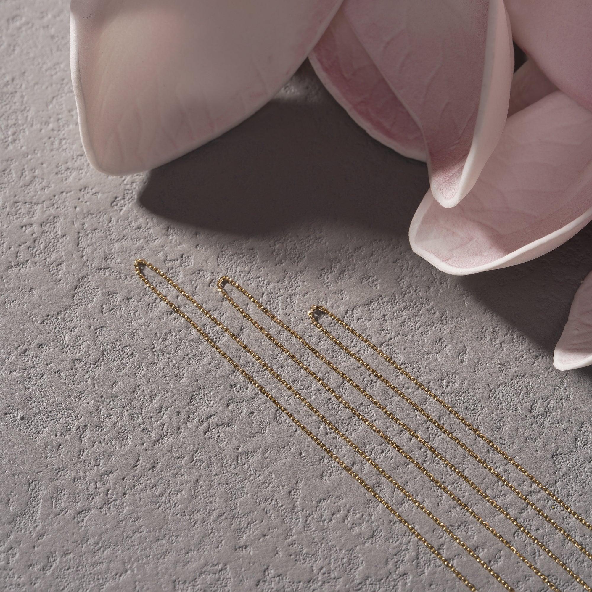 Delicate gold chain necklaces on textured surface with soft pink flower petals