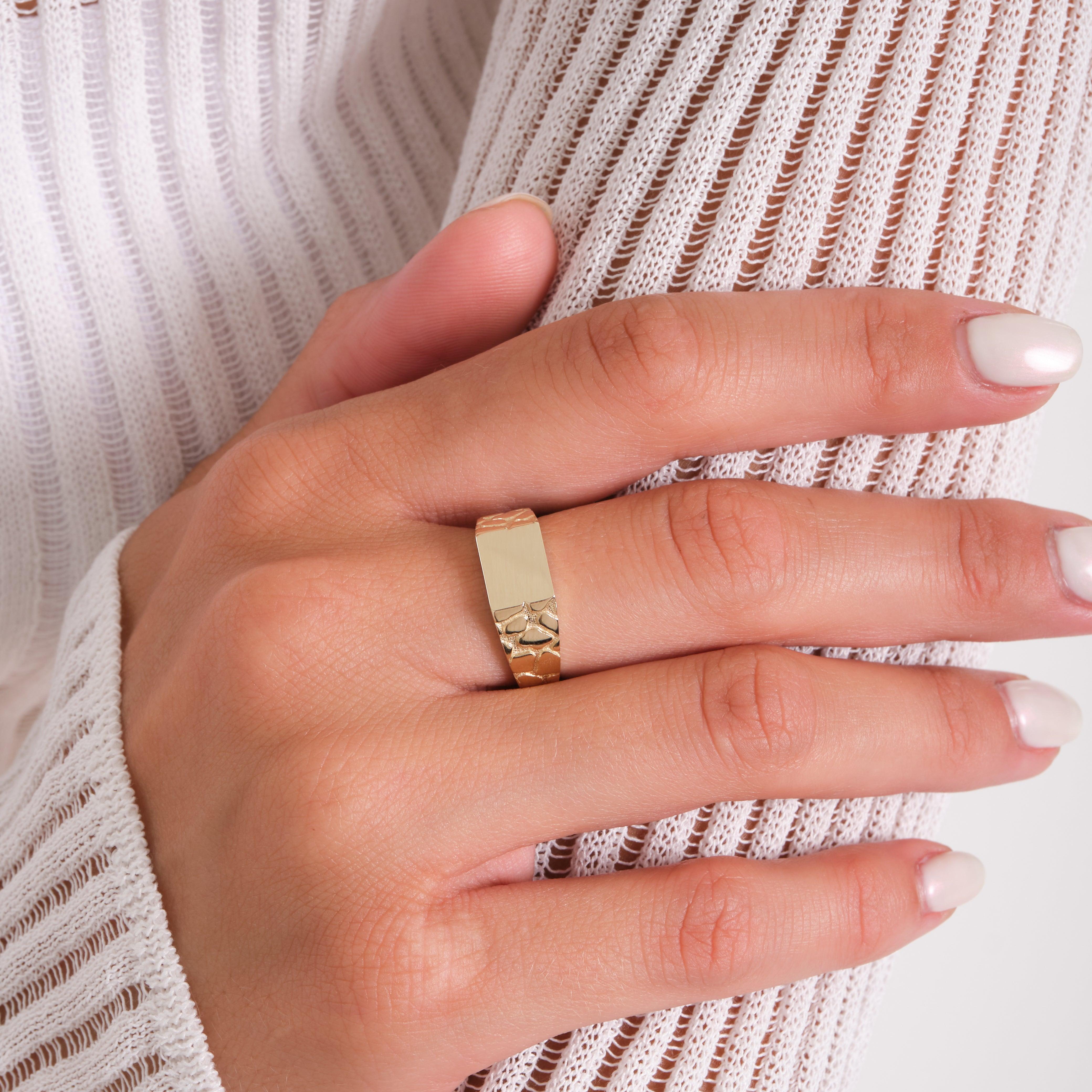 Close-up of a hand wearing a textured gold ring with a blank rectangular face