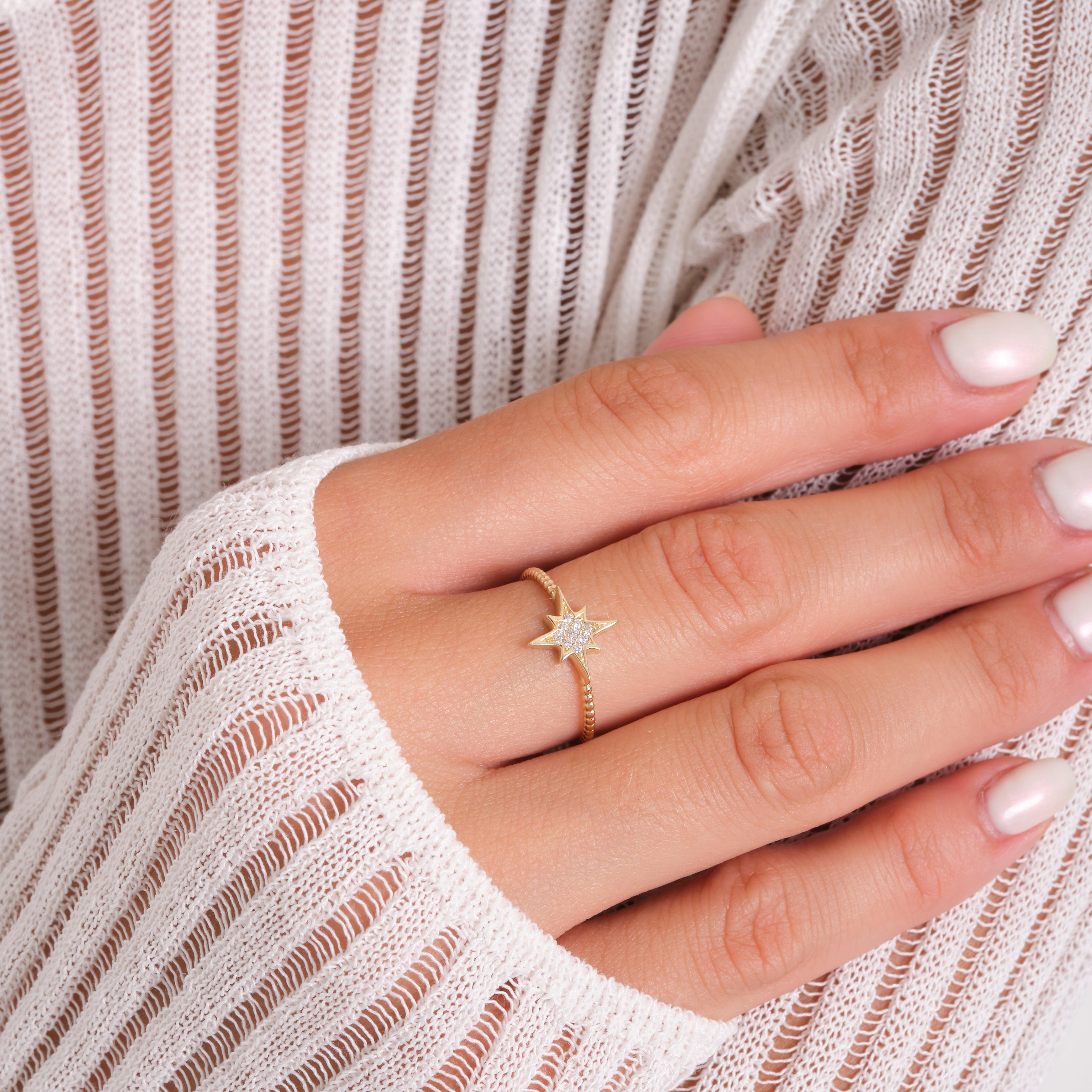 Gold star-shaped ring with small diamonds on a hand, white striped sweater background