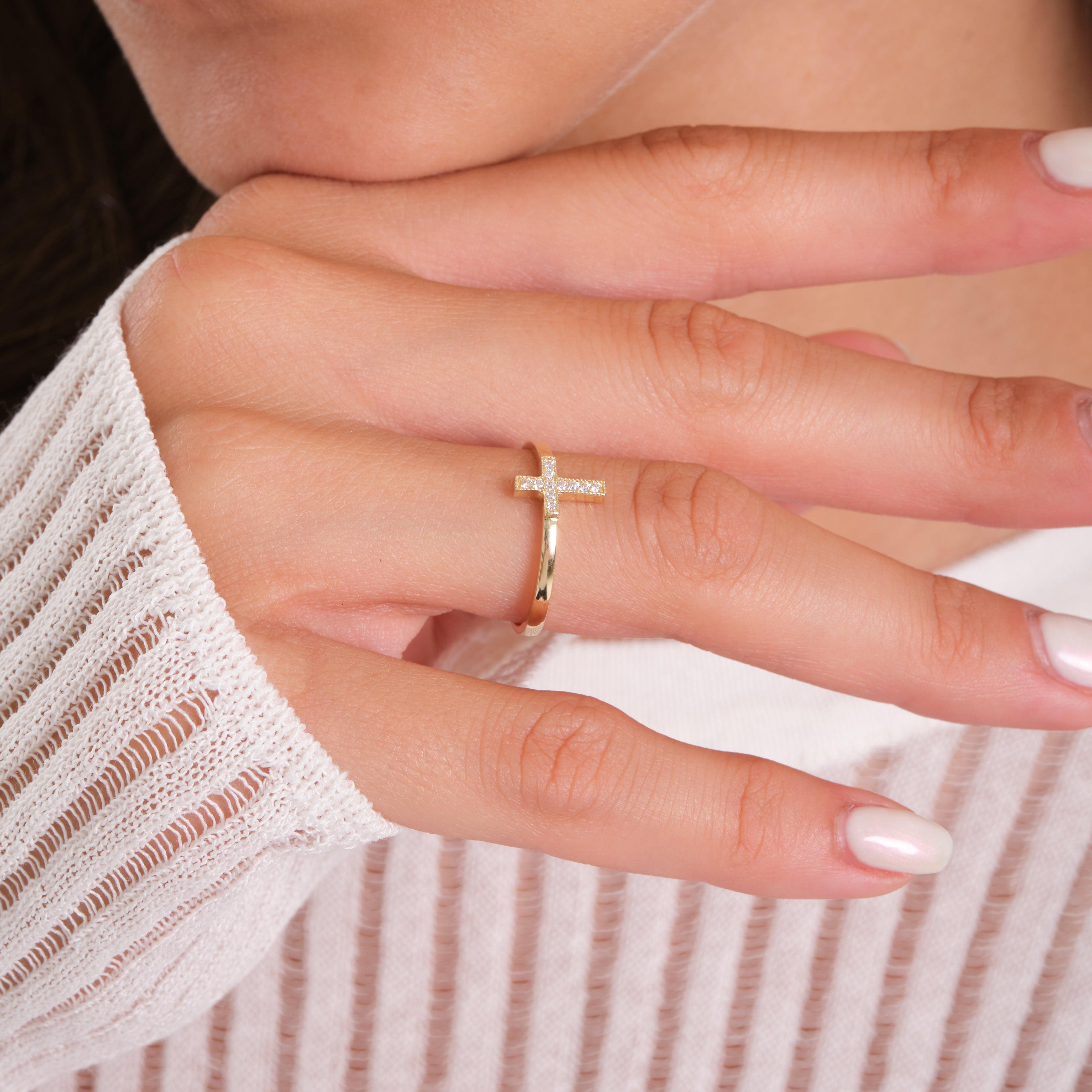 Gold cross ring with small diamonds on woman's hand, minimalist jewelry style