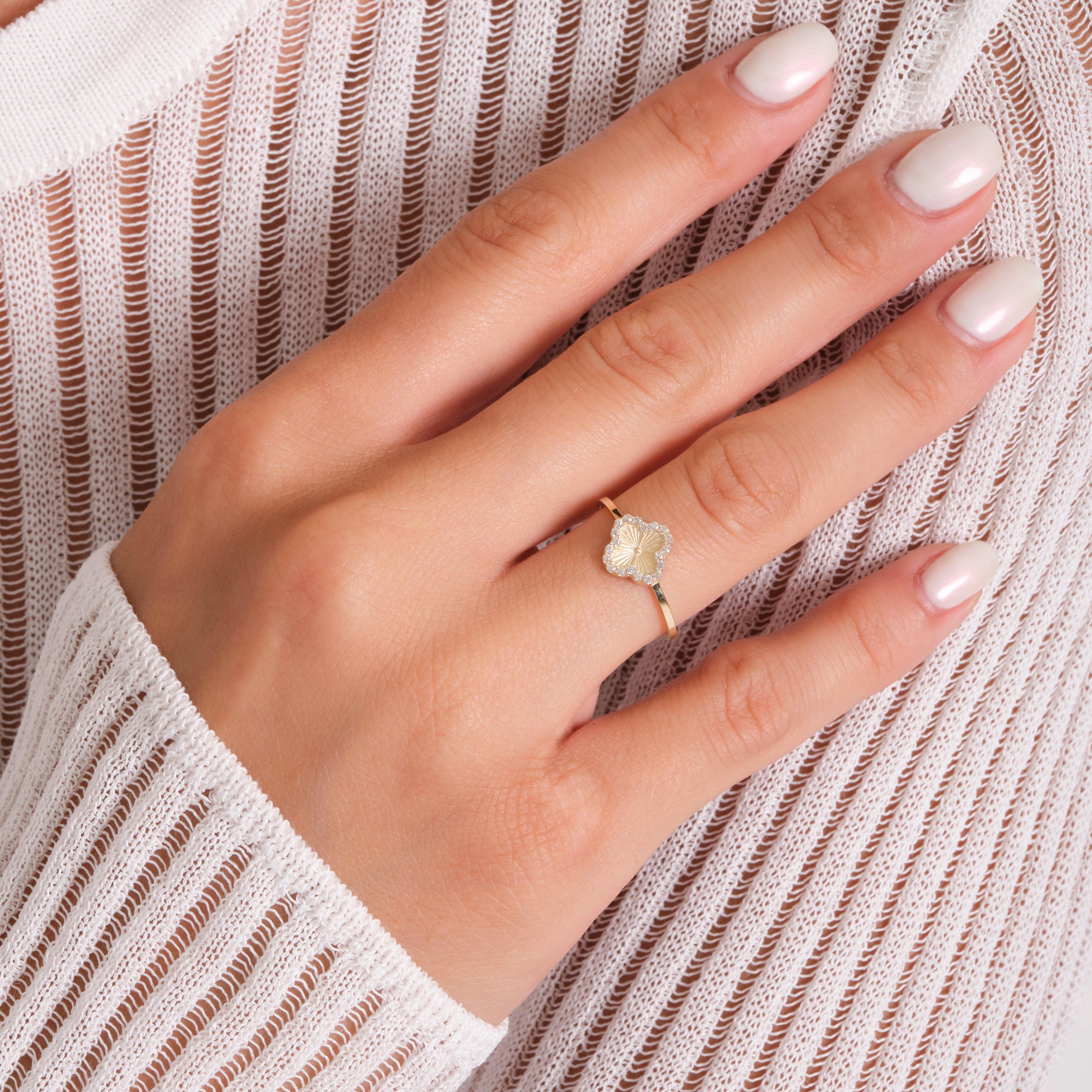 Woman’s hand wearing delicate gold flower ring, white striped sweater background