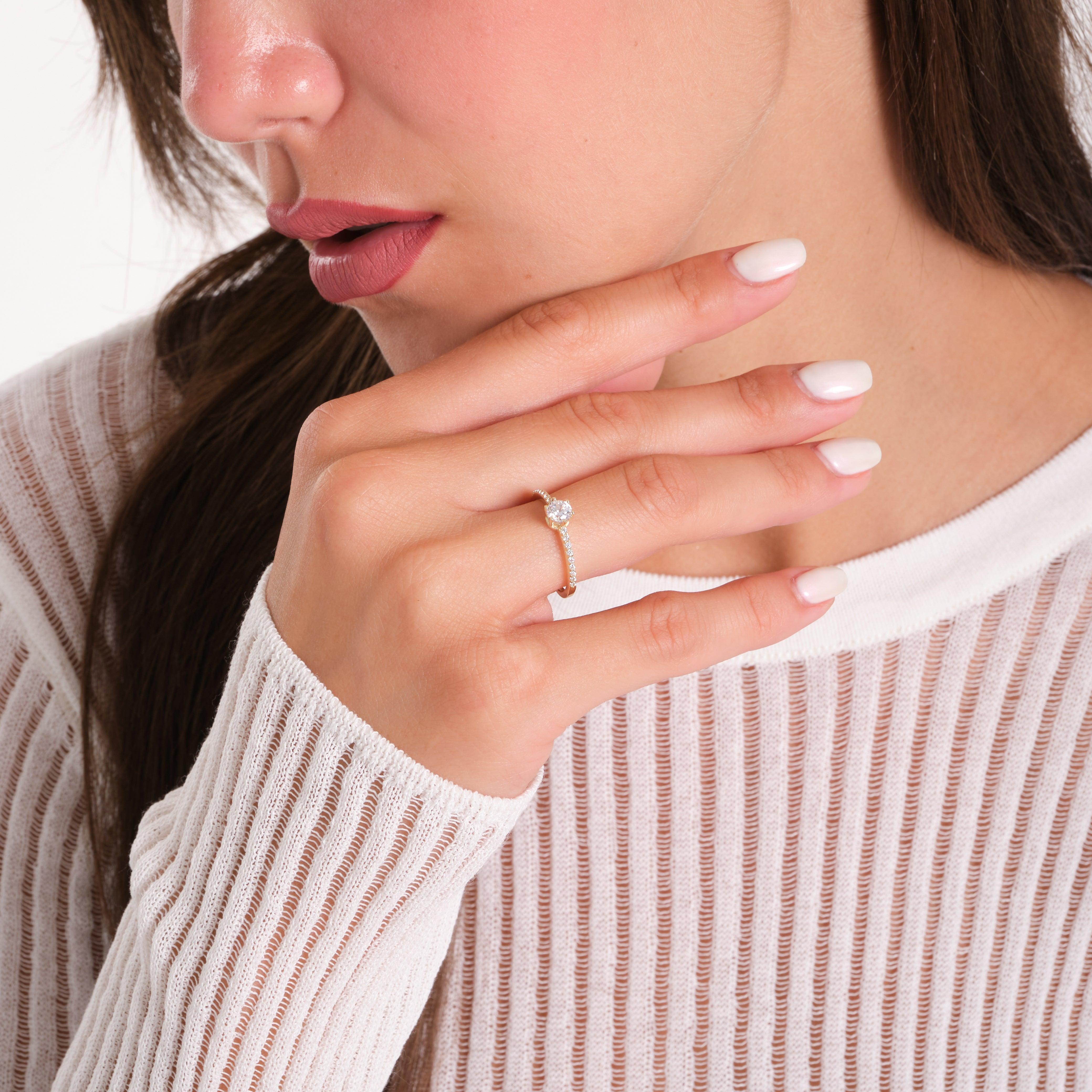 Woman wearing a gold diamond ring, hand near face, in a white textured top