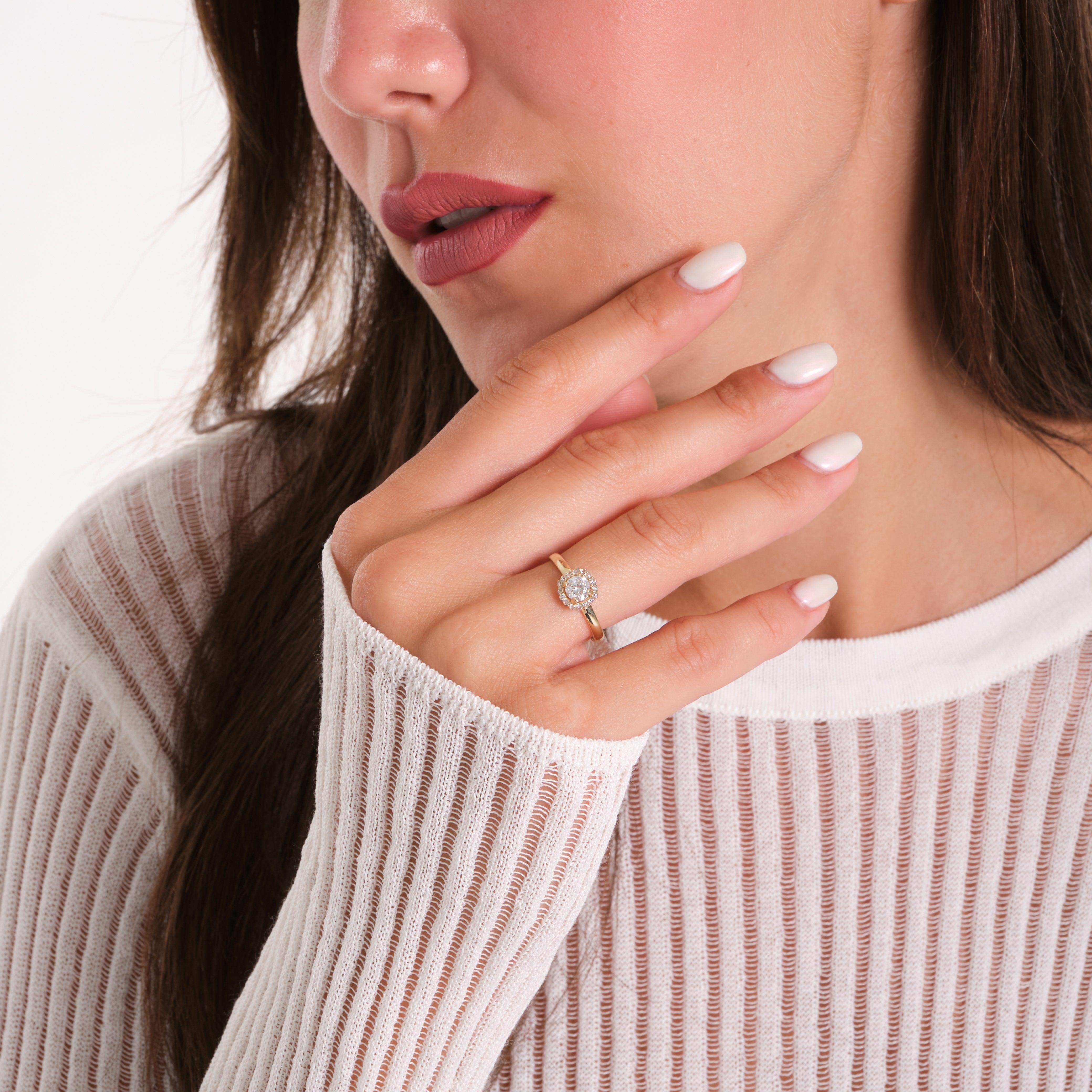 Woman wearing a gold ring with a round diamond halo setting on her finger