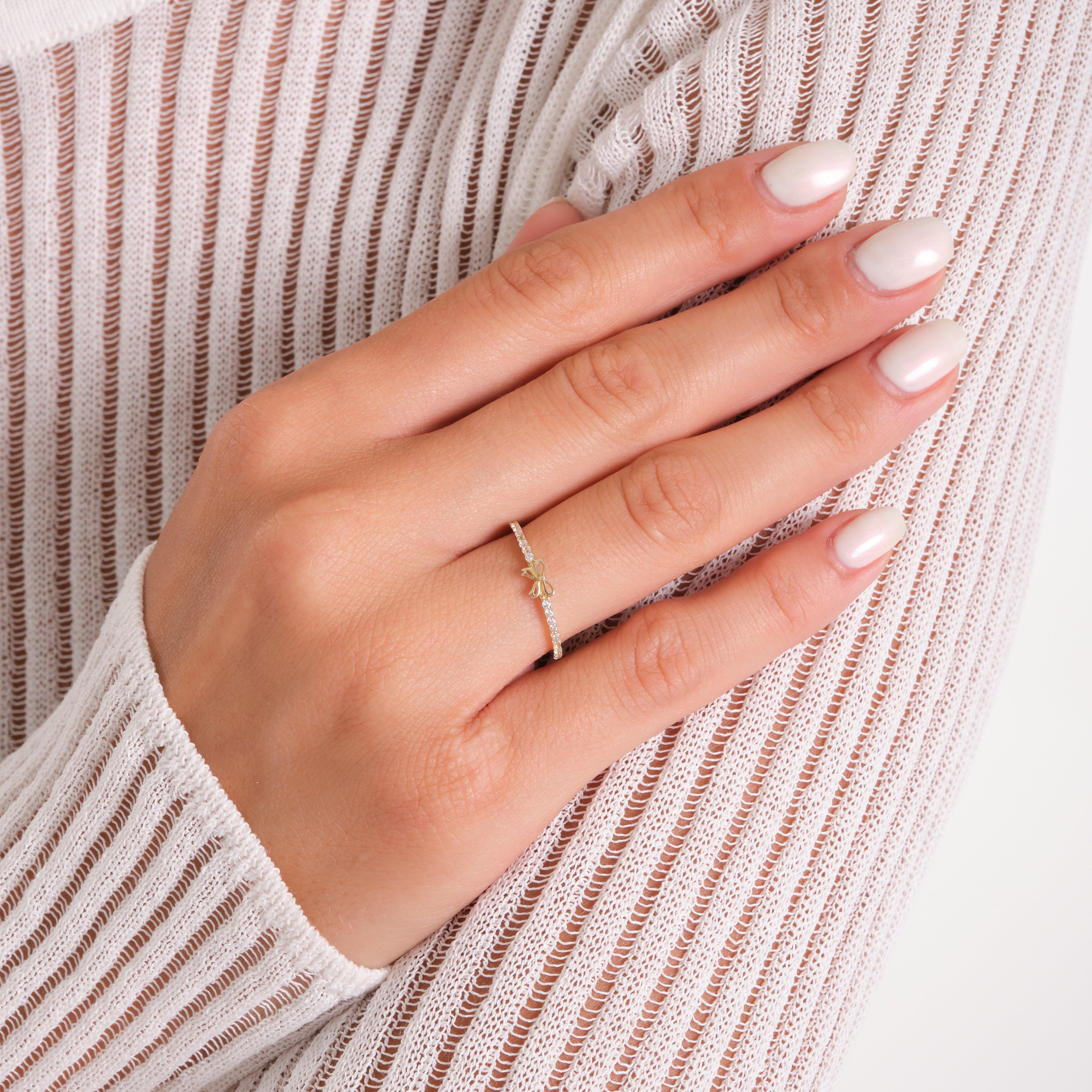 Delicate gold ring with small gemstone on woman's hand, white knit sleeve background