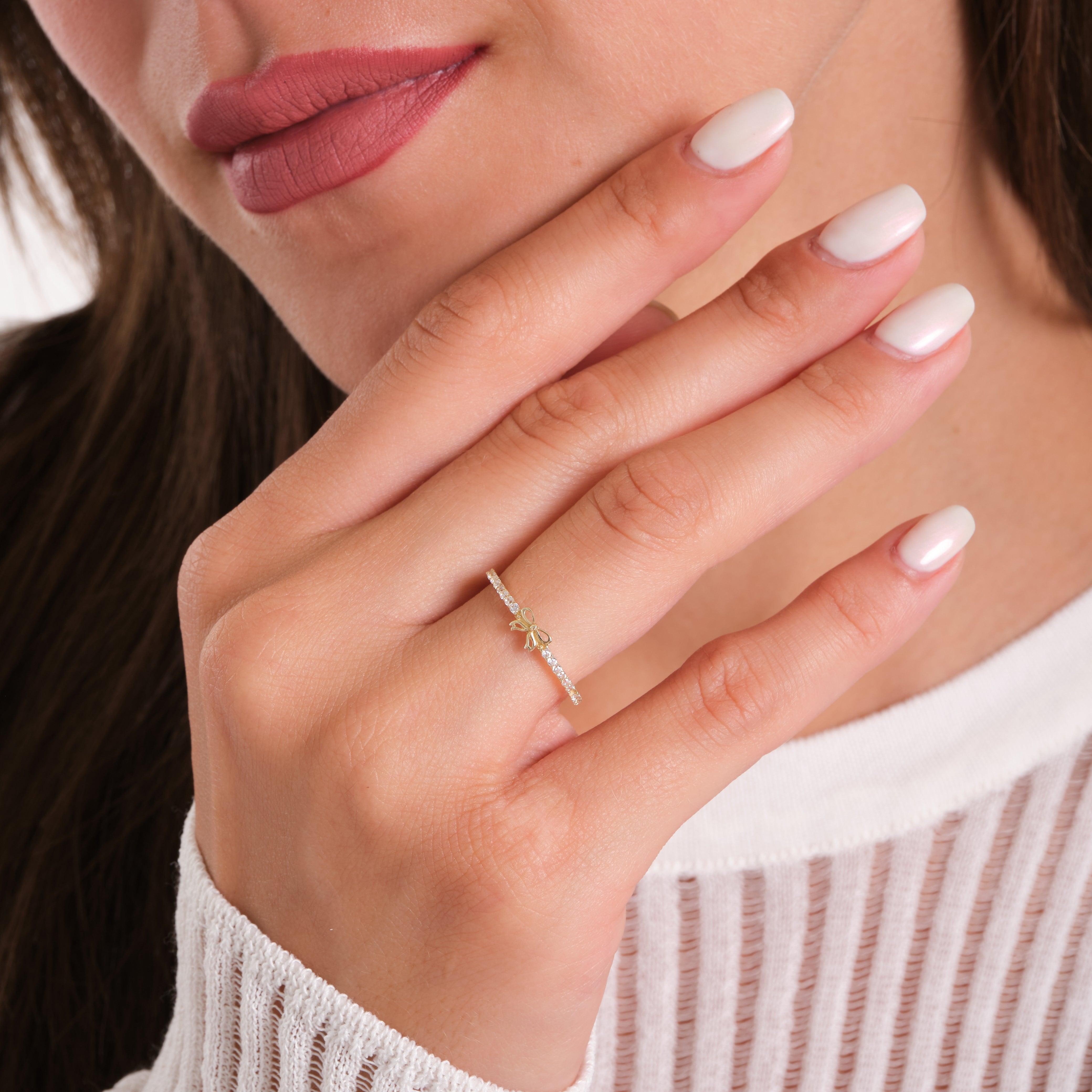 Woman wearing a delicate gold ring with bow design and clear stones on manicured hand