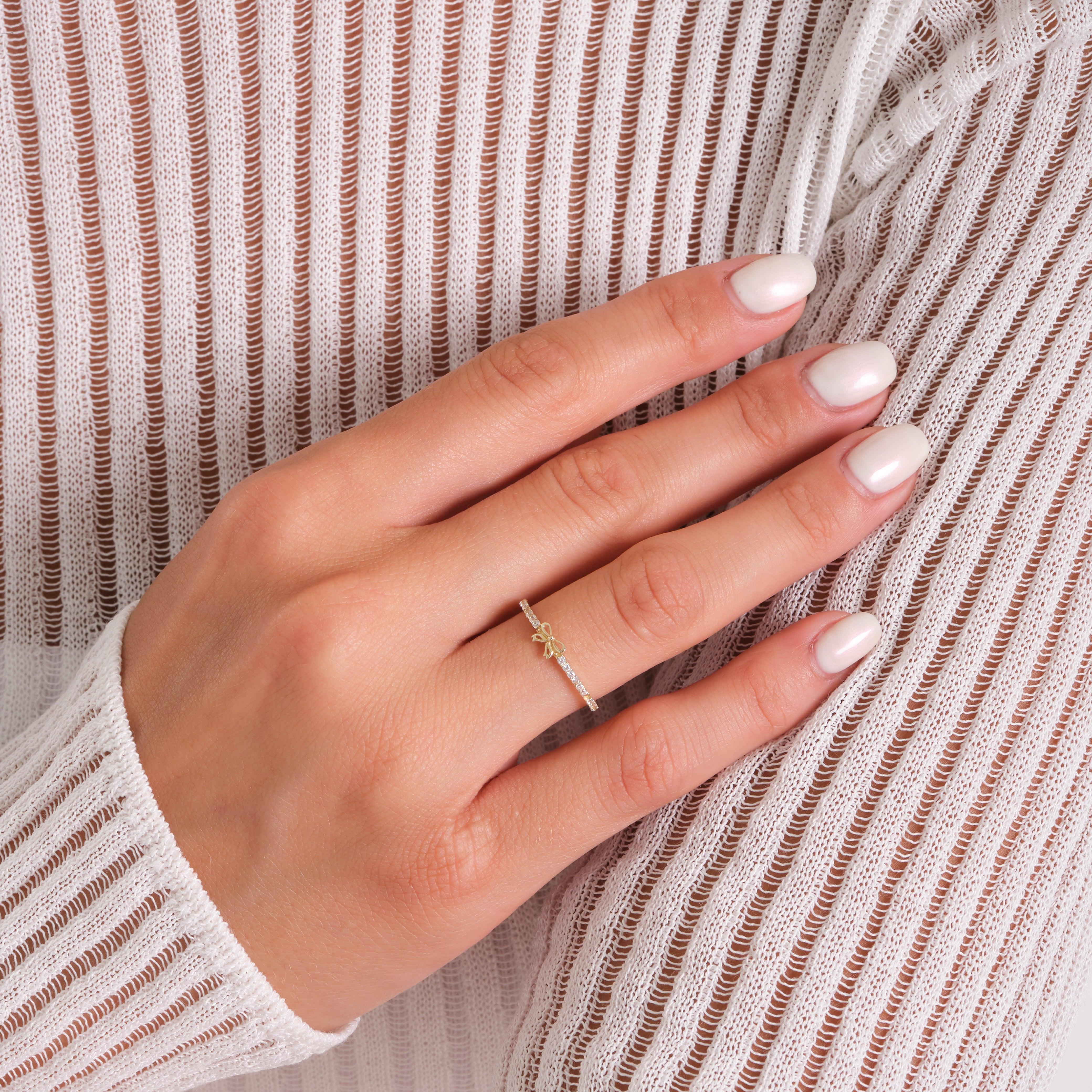 Delicate gold ring with bow detail on woman's hand against a white textured top.