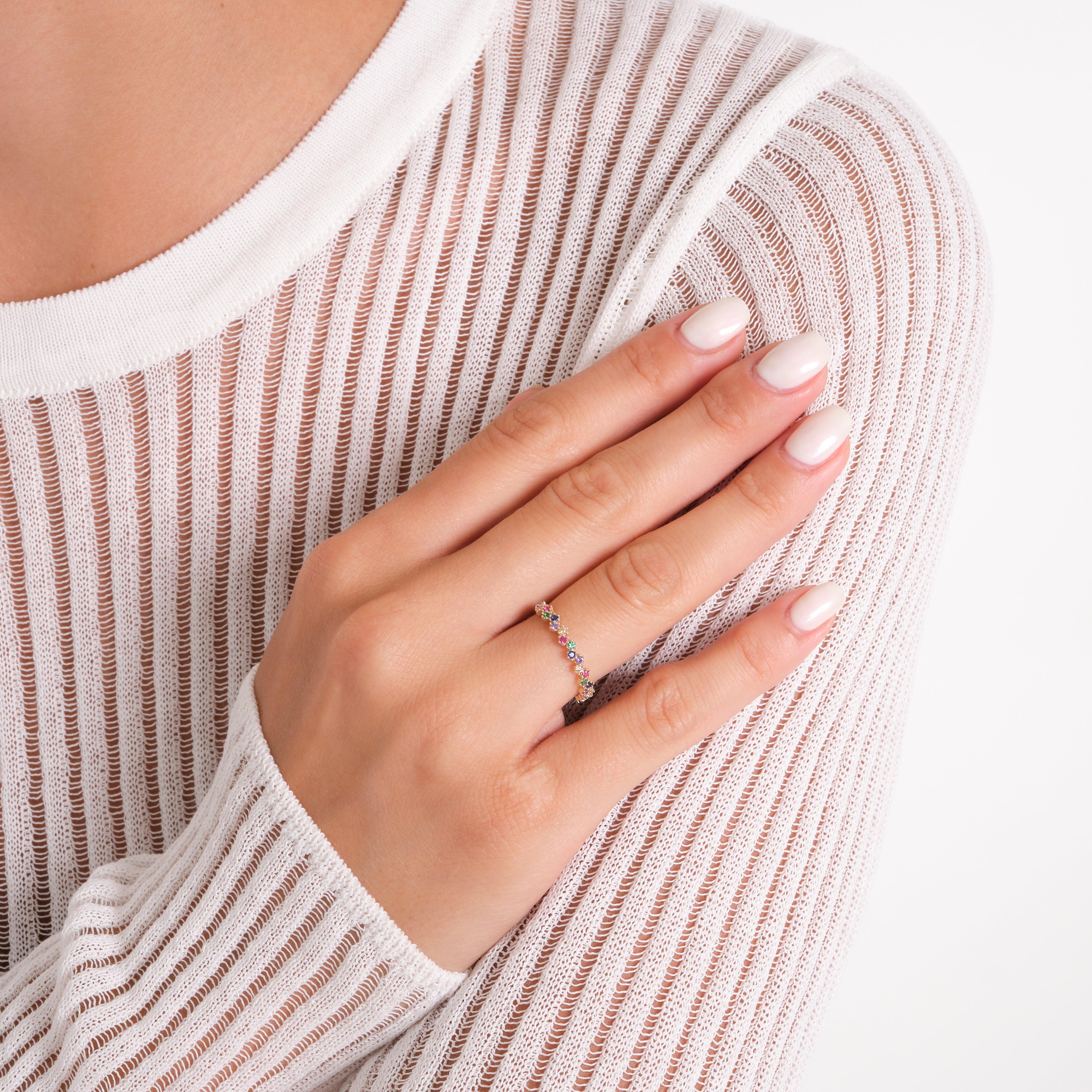 Hand wearing a delicate gold ring with multicolored gemstones, white striped top