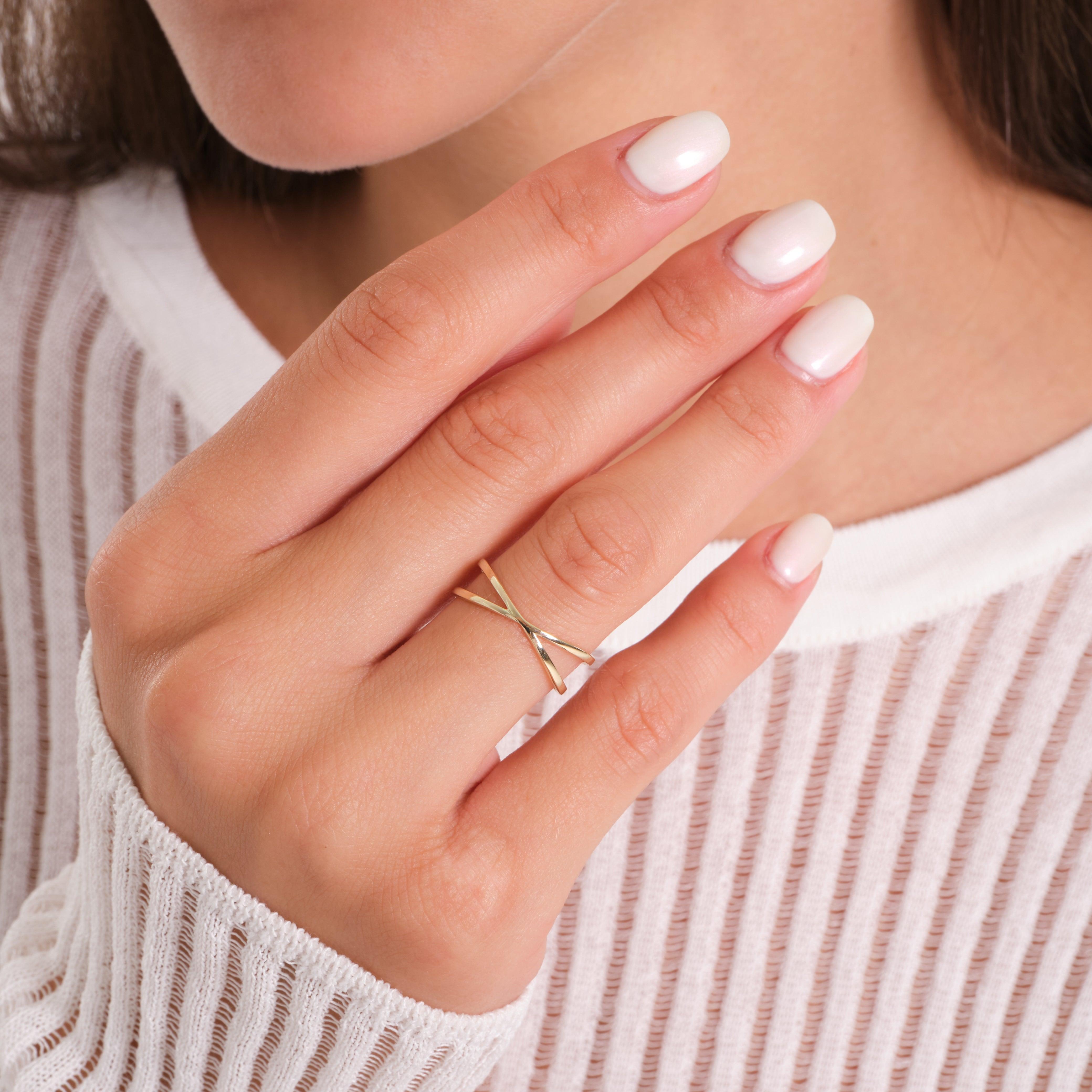 Woman wearing a delicate gold criss-cross ring with manicured nails