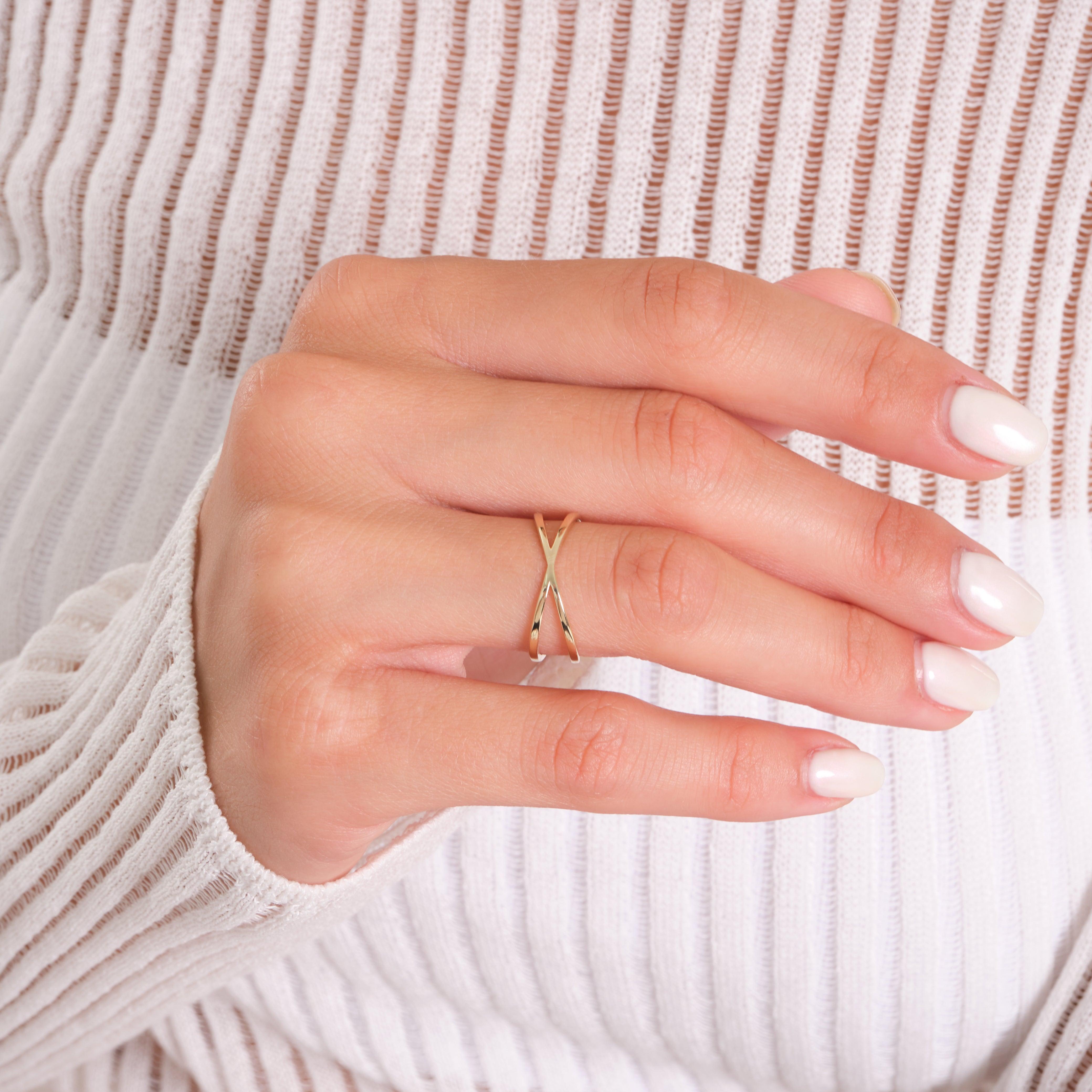 Minimalist gold ring with criss-cross design on hand, white textured sweater background