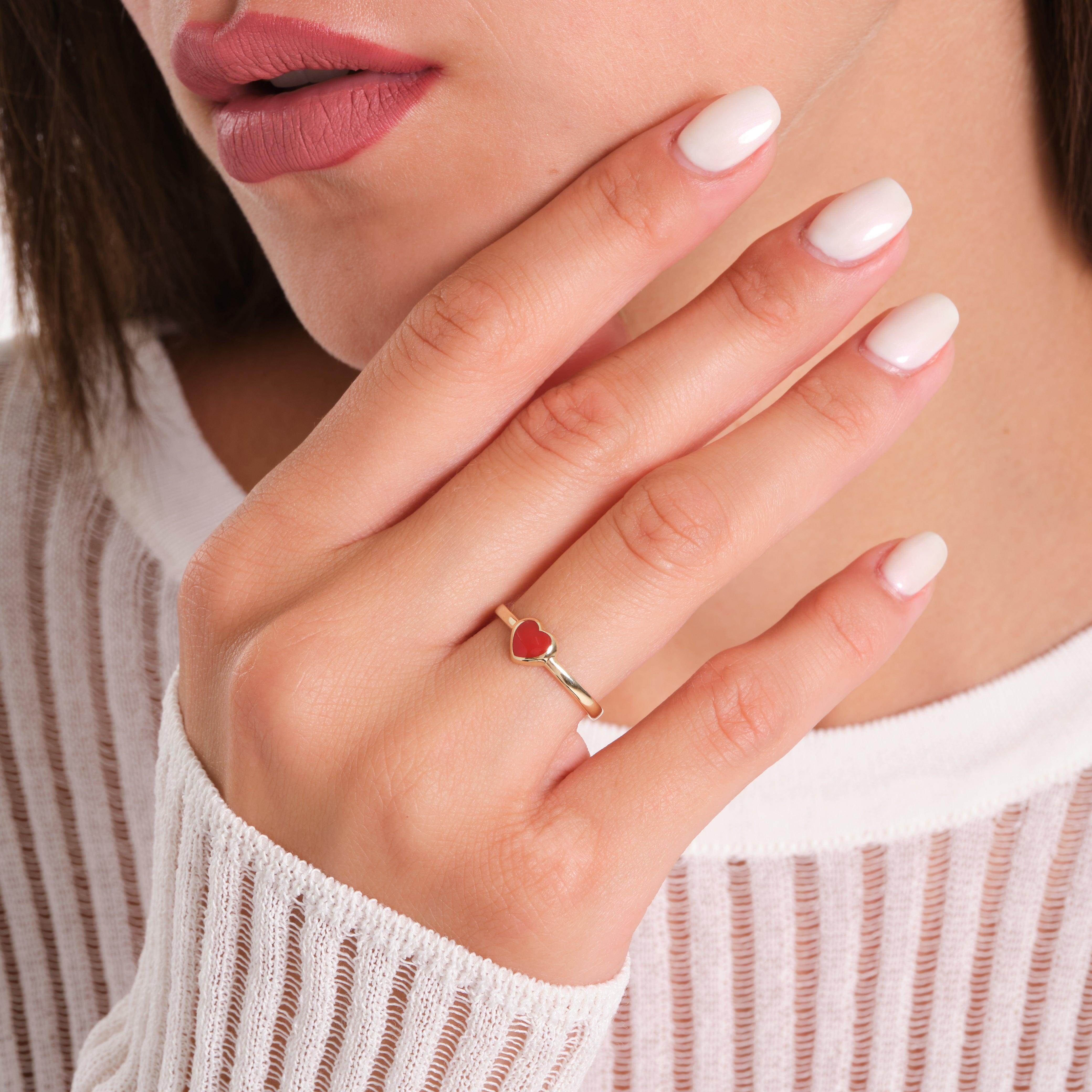 Woman wearing a gold ring with a red heart gemstone, manicured nails, white top