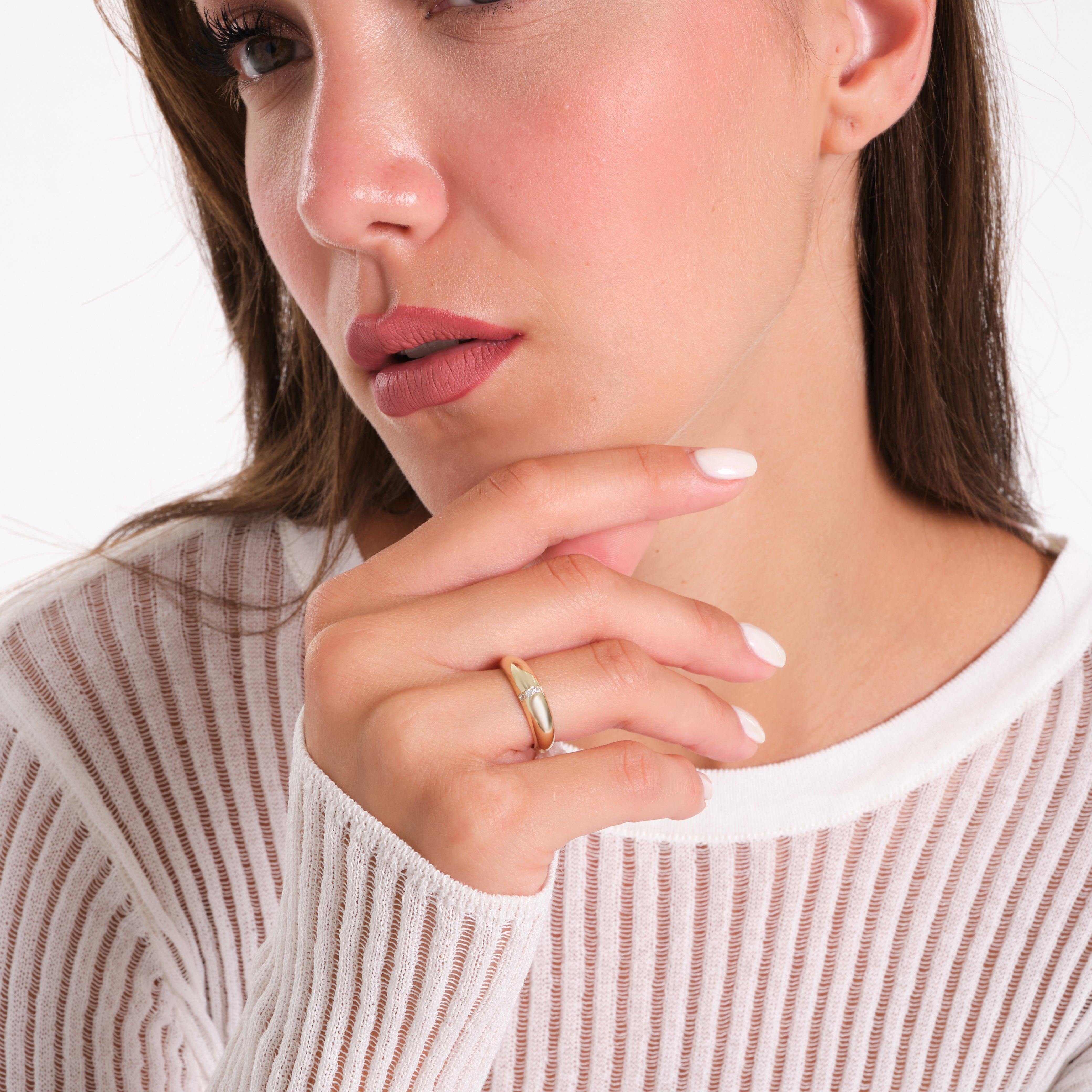 Woman wearing a gold ring with a diamond accent, close-up hand and face, white top