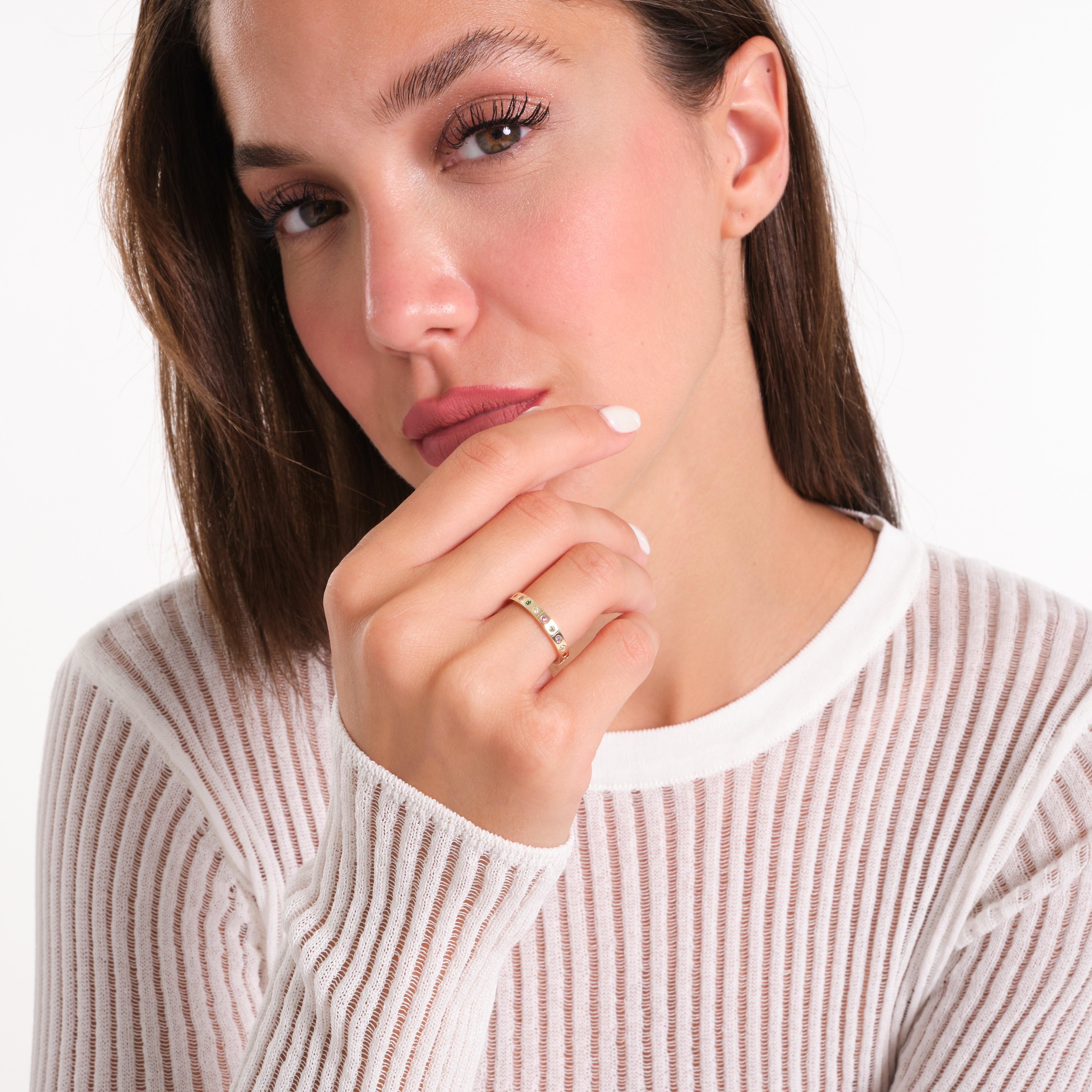 Woman wearing a gold ring with gemstones, white mesh top, close-up jewelry display