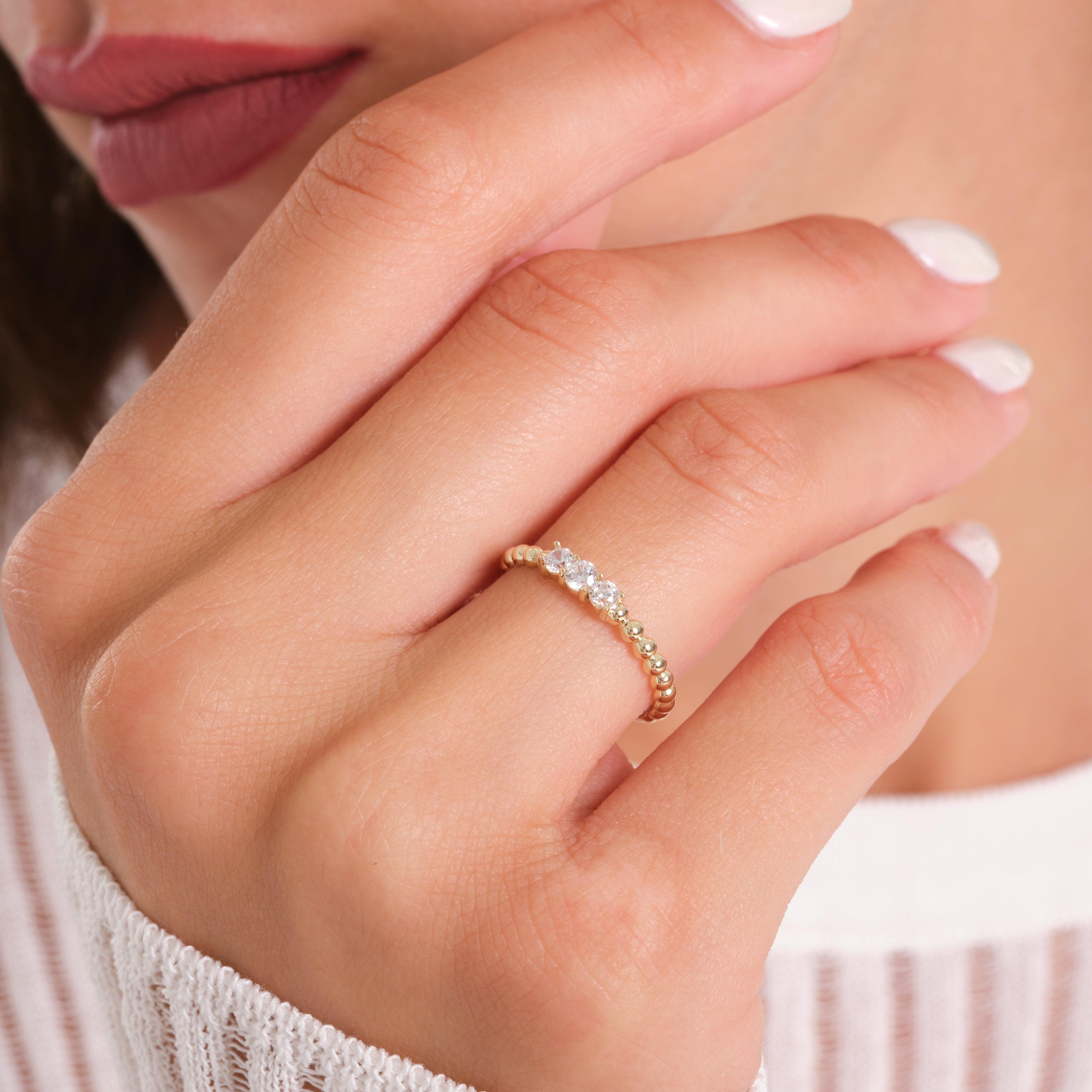 Gold beaded ring with three clear gemstones worn on a woman's hand