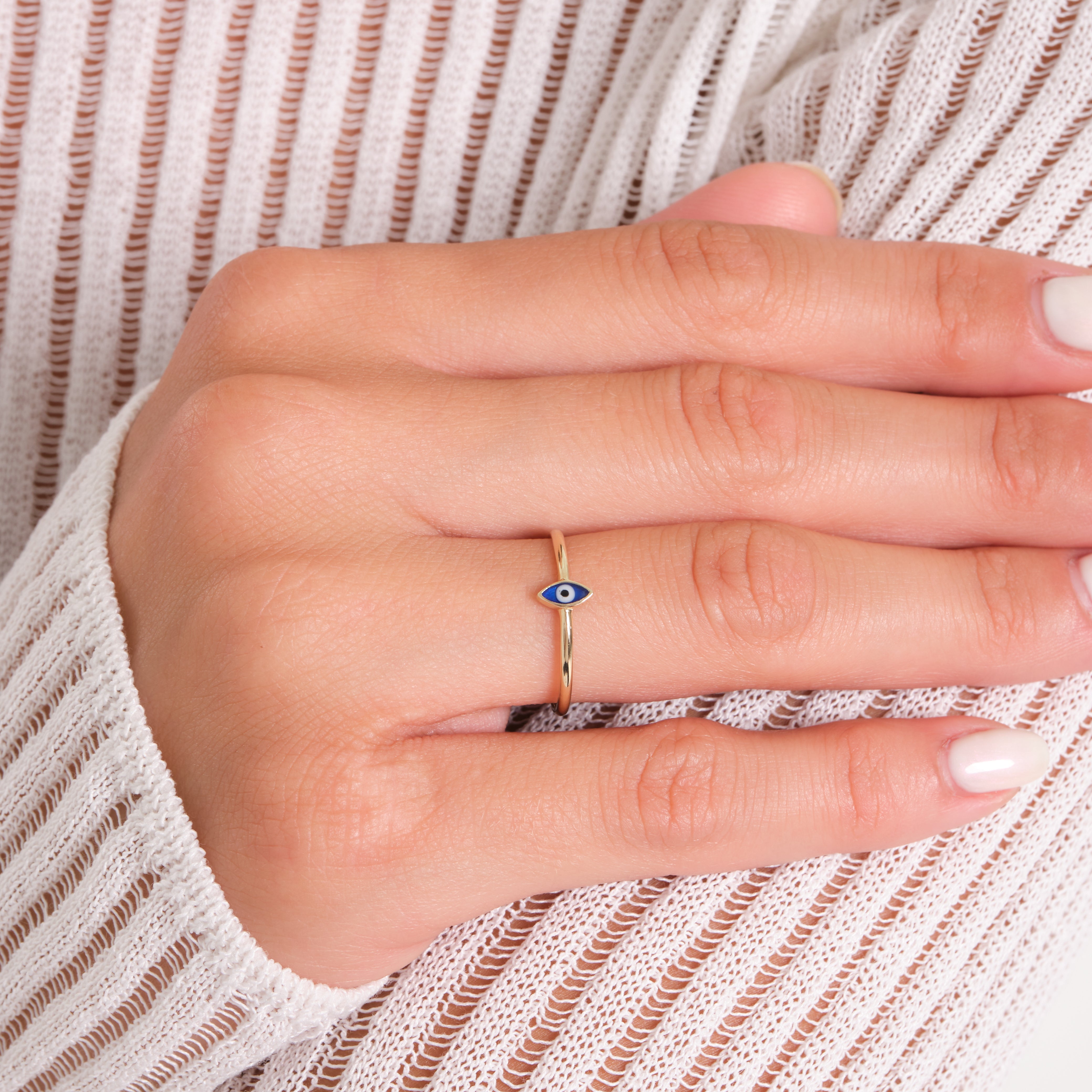 Hand wearing a gold ring with a blue eye design on a white background