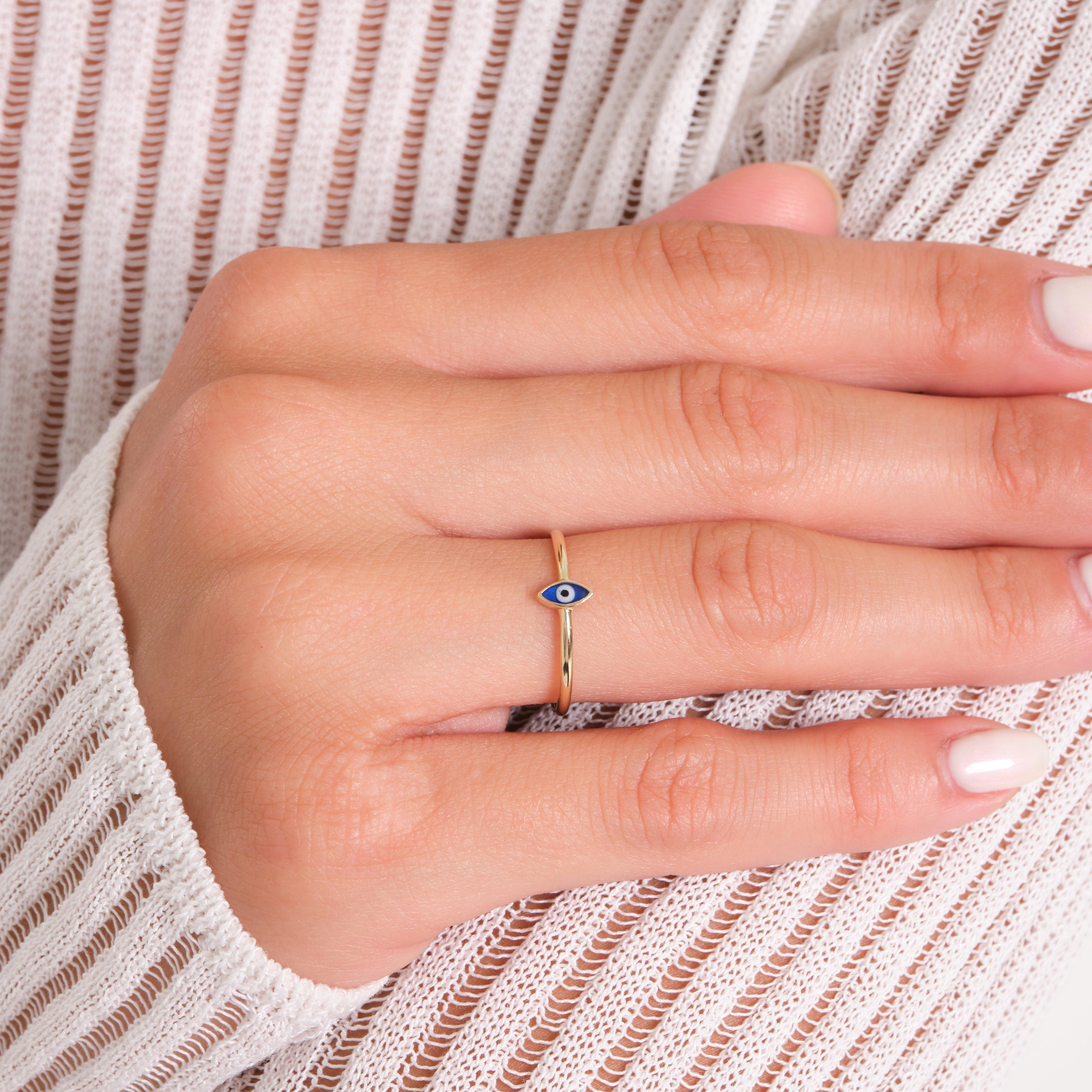 Gold evil eye ring on hand with white knit sleeve, delicate gold jewelry