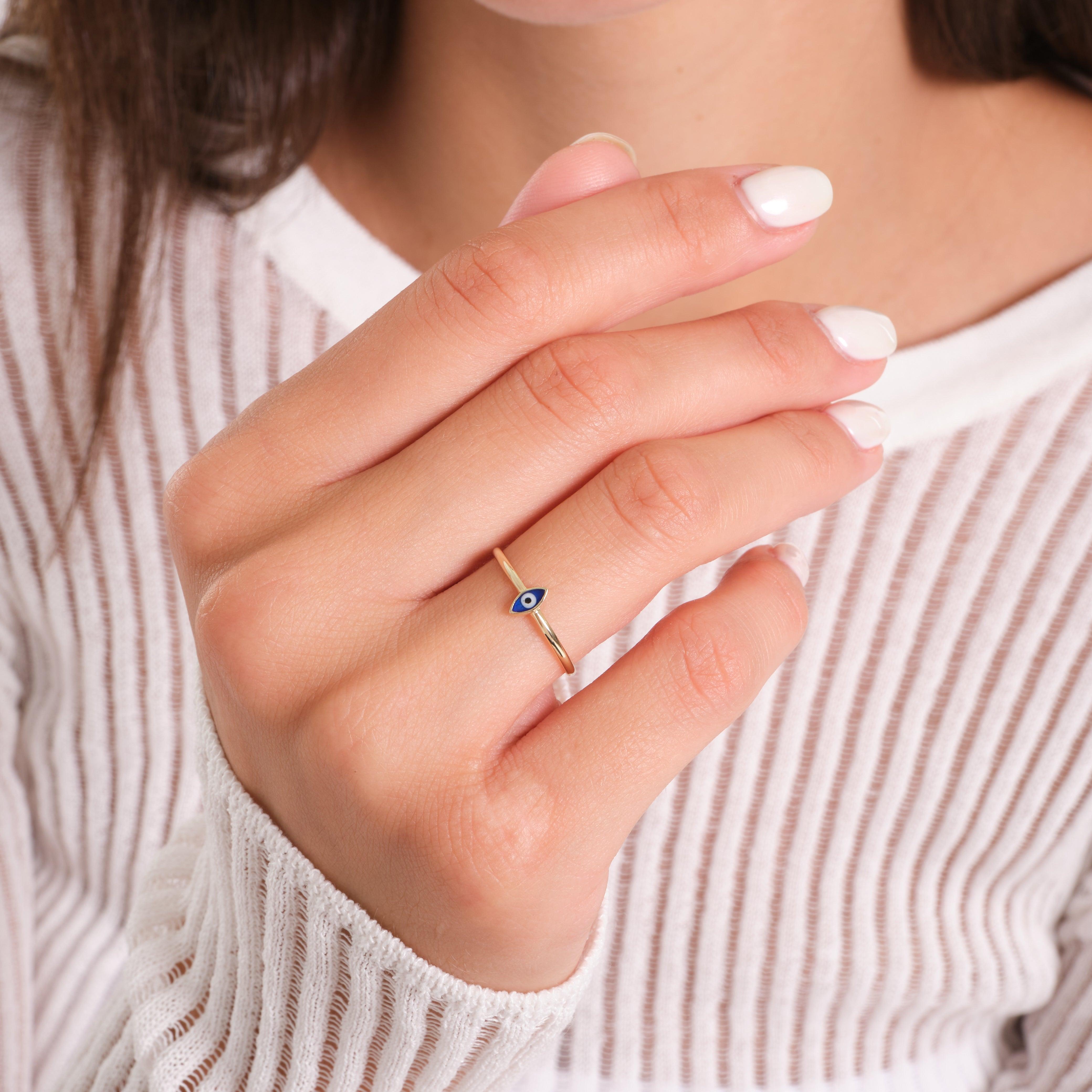 Gold evil eye ring on woman's hand, delicate jewelry with blue enamel detail