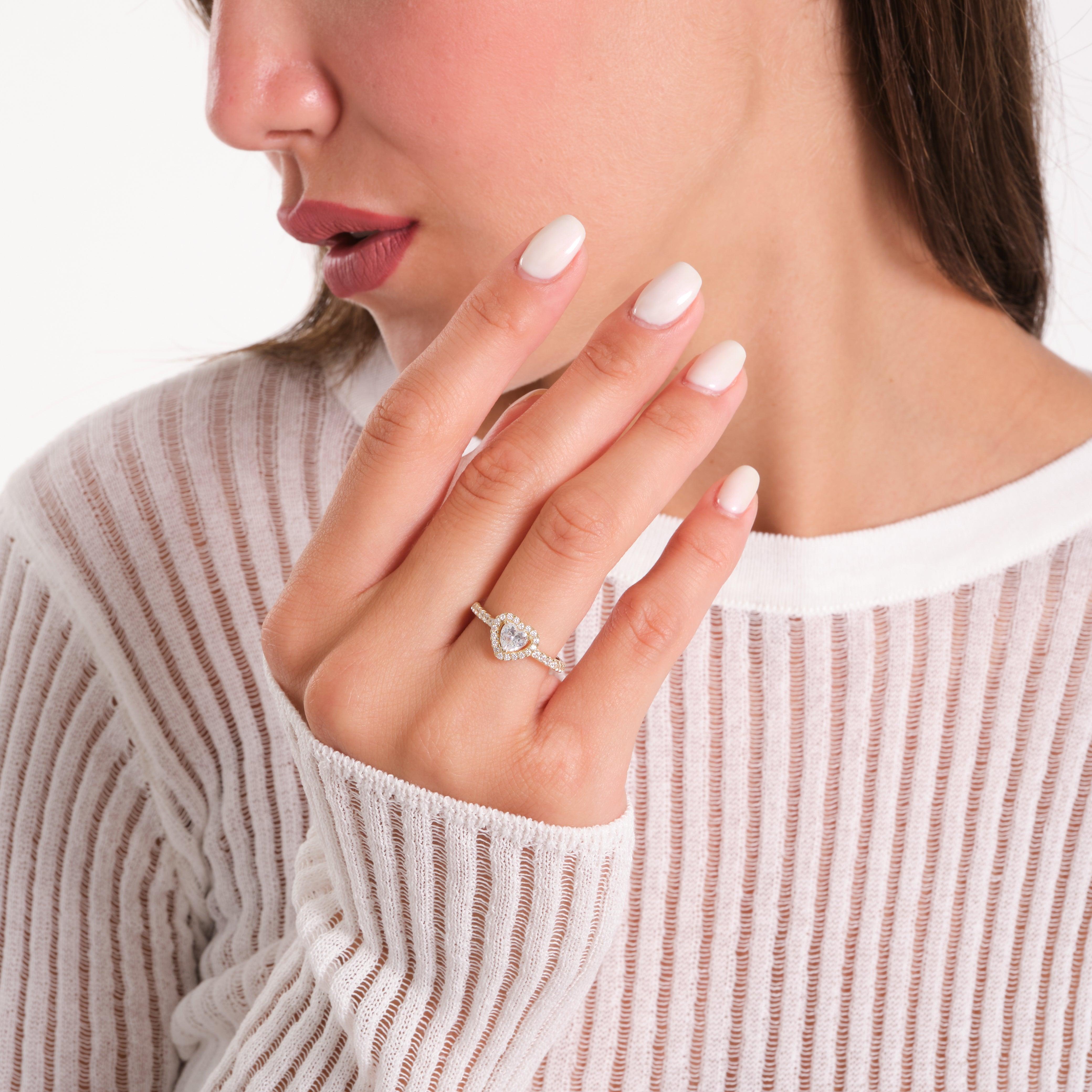 Woman wearing a gold diamond ring on her finger, dressed in a white mesh top