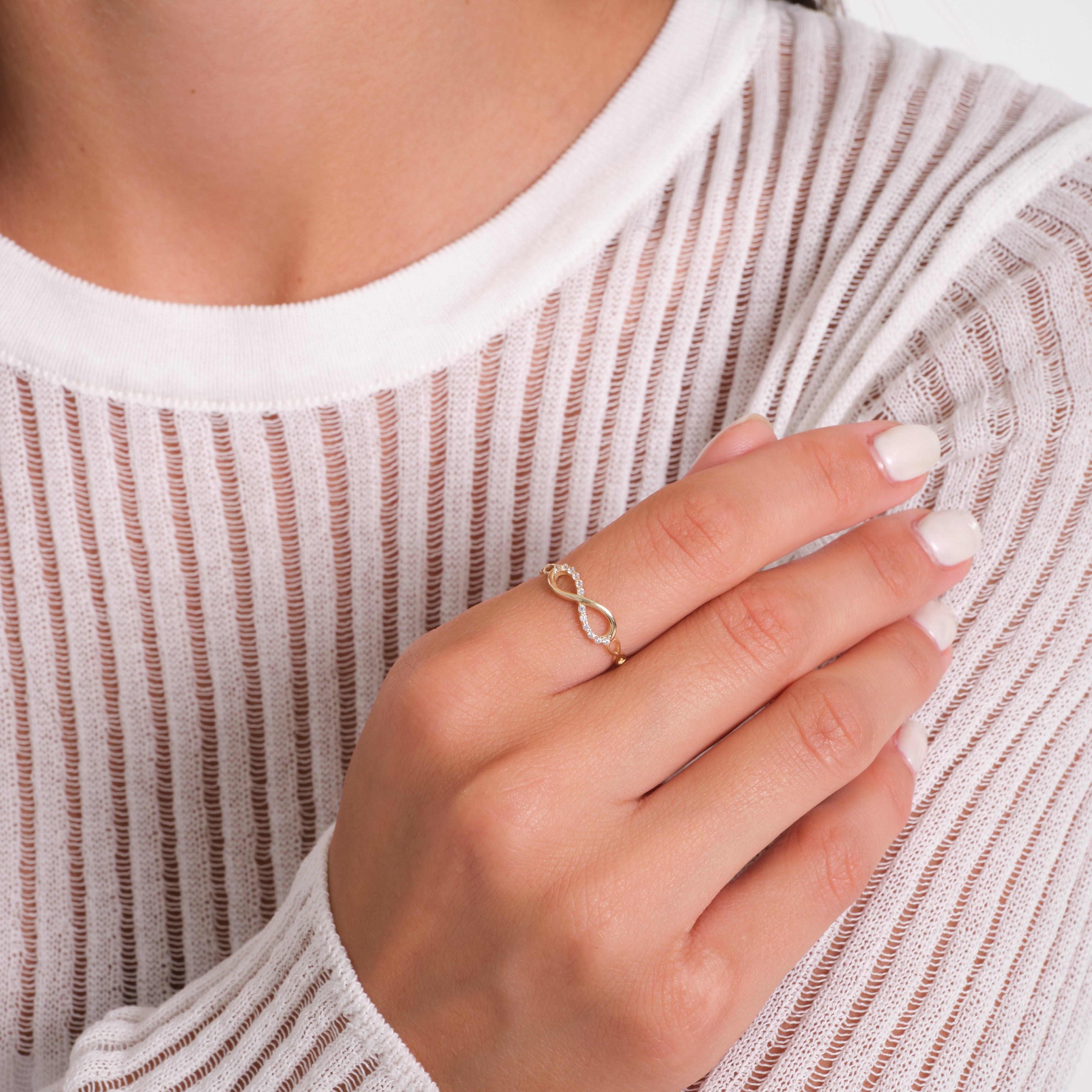 Gold infinity ring with small diamonds on woman's hand against white textured top