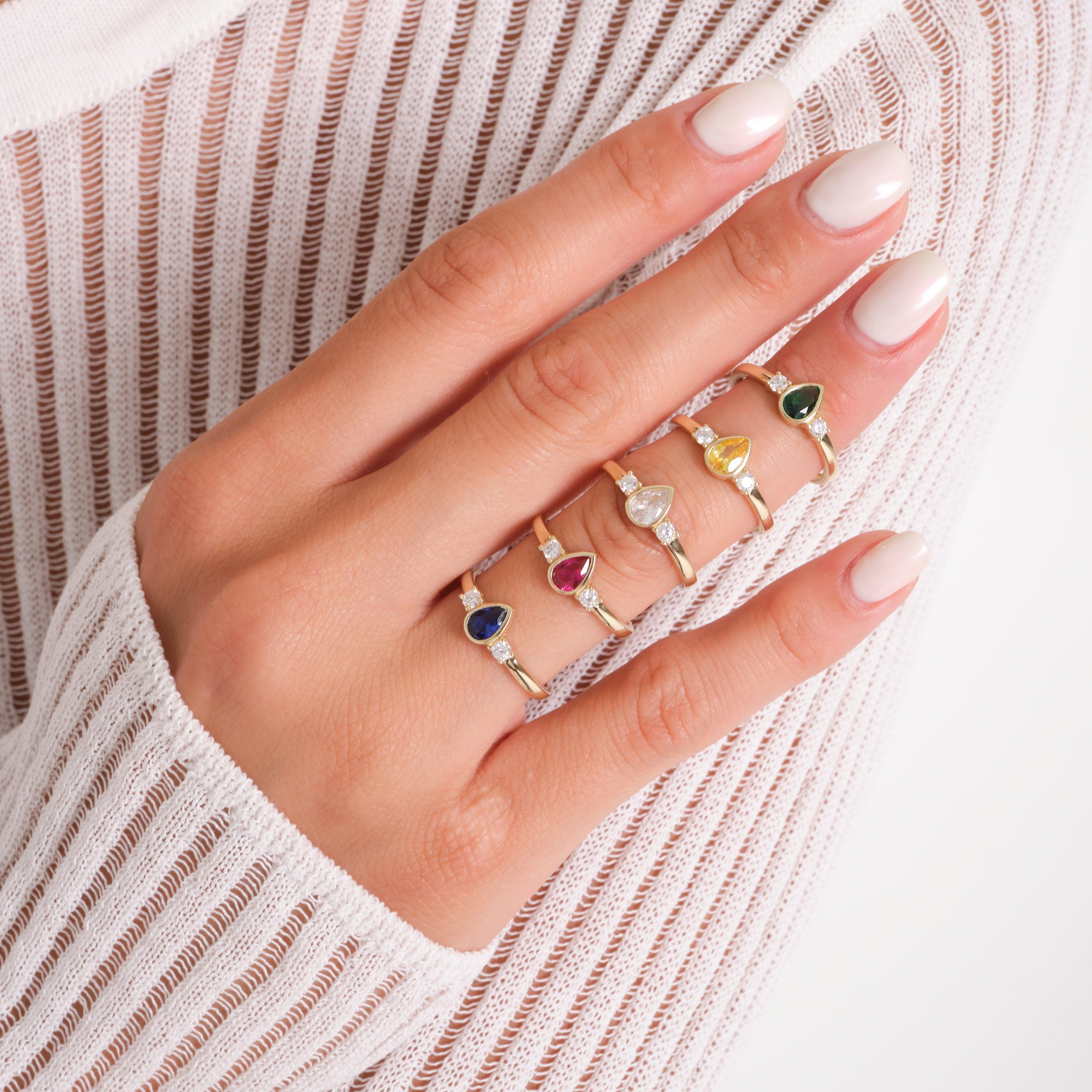Hand wearing gold rings with colorful gemstone and diamond accents, elegant nail design