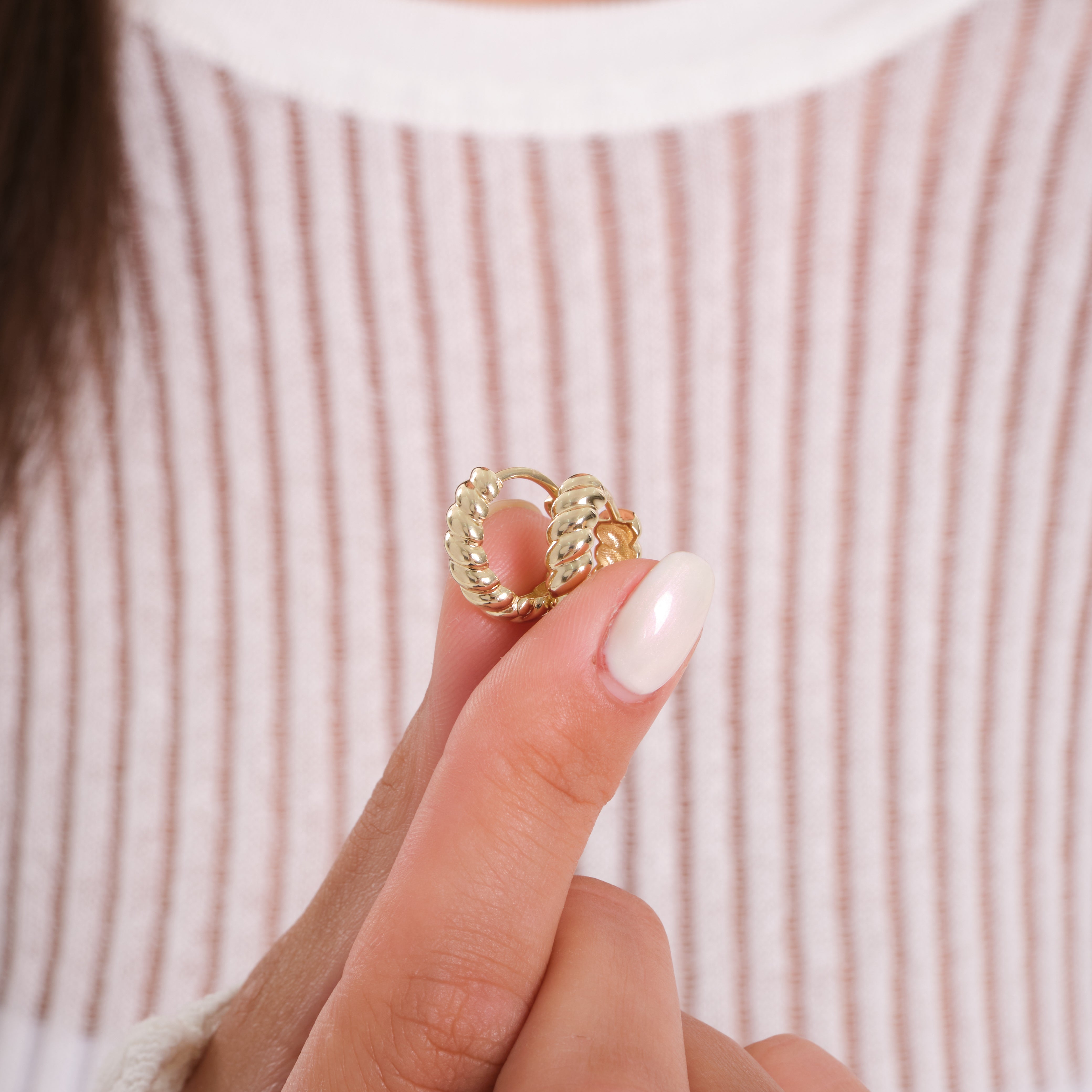 Gold ring held between fingers against a striped background