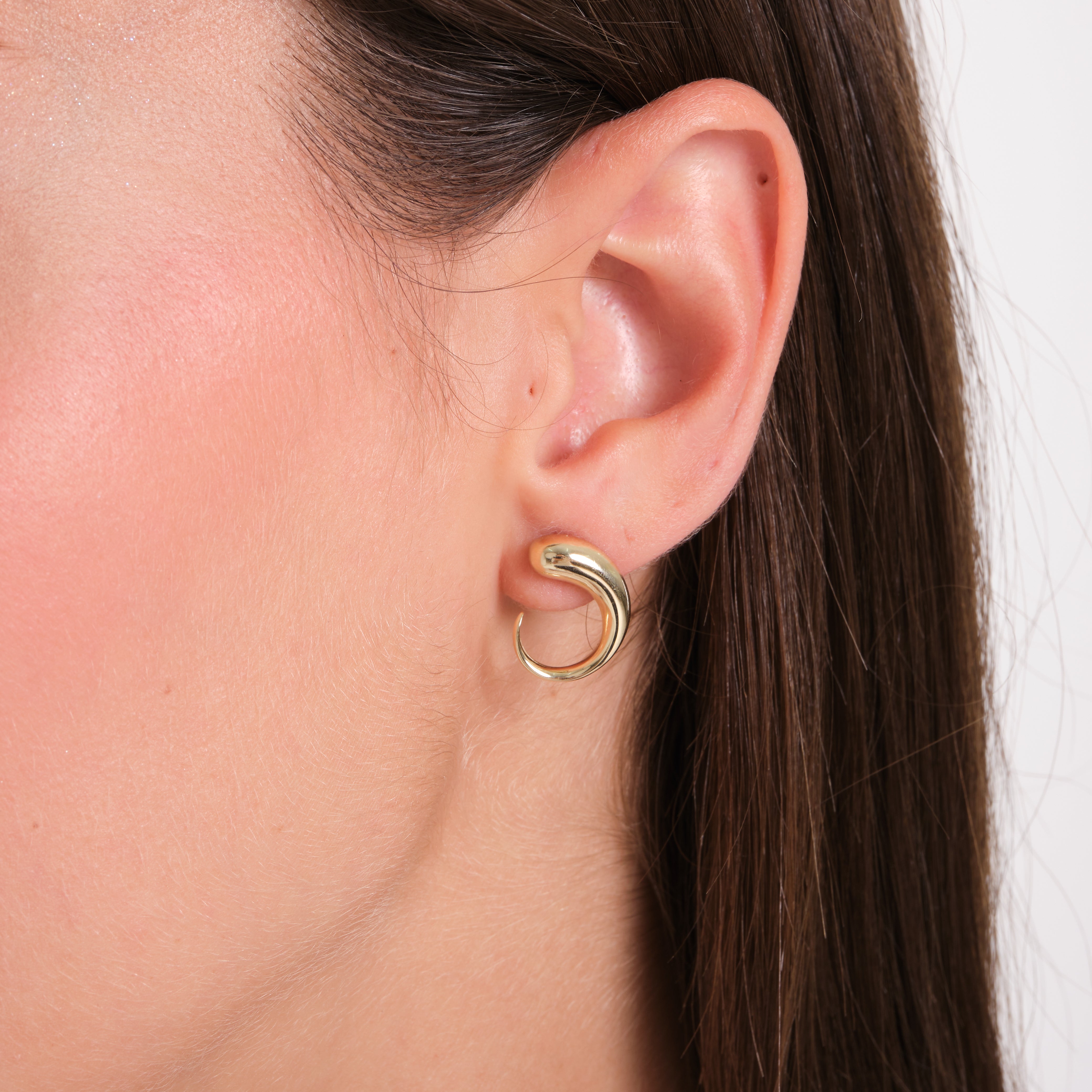 Gold hoop earring worn by a person with brown hair.