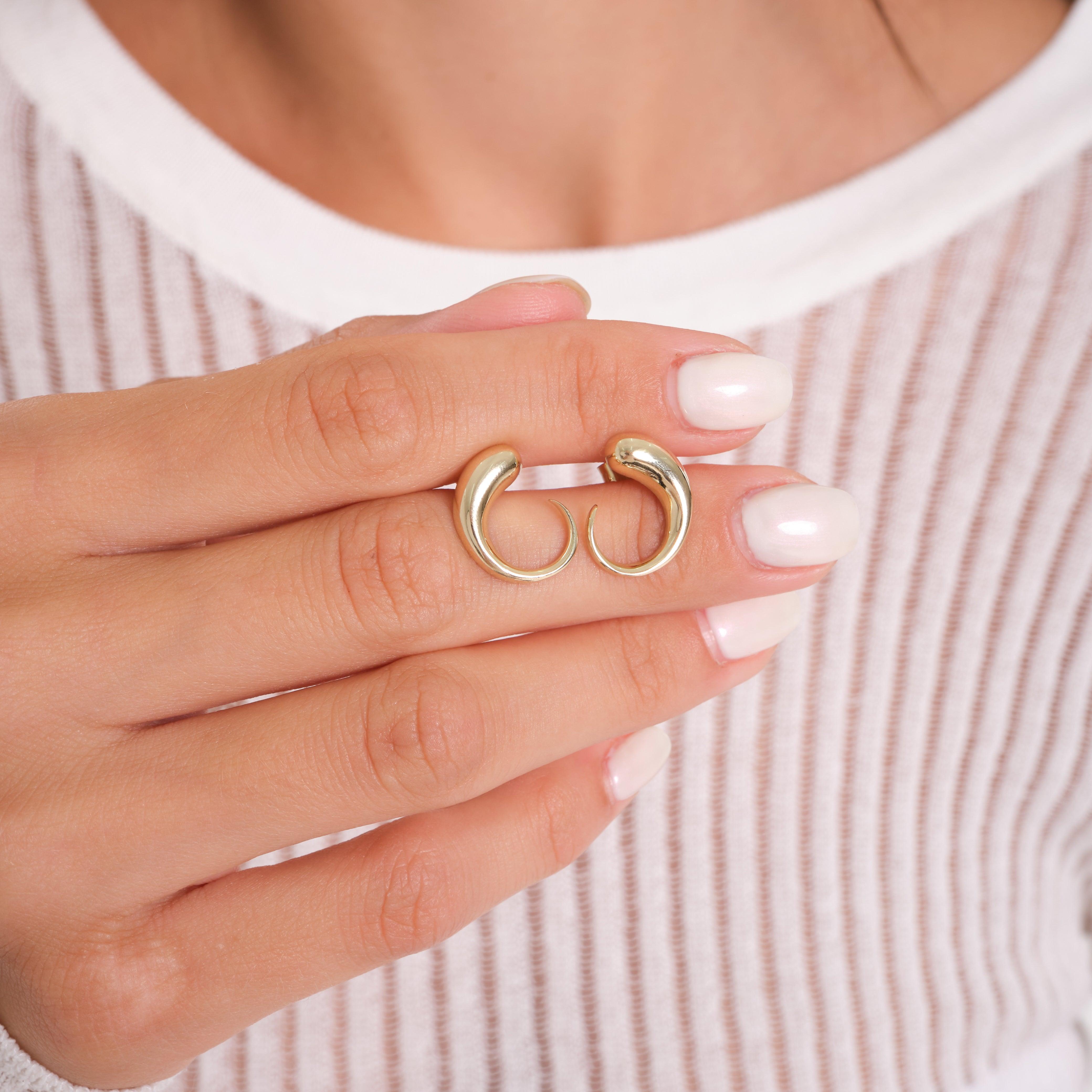 Woman holding a pair of gold hoop earrings with a modern, curved design