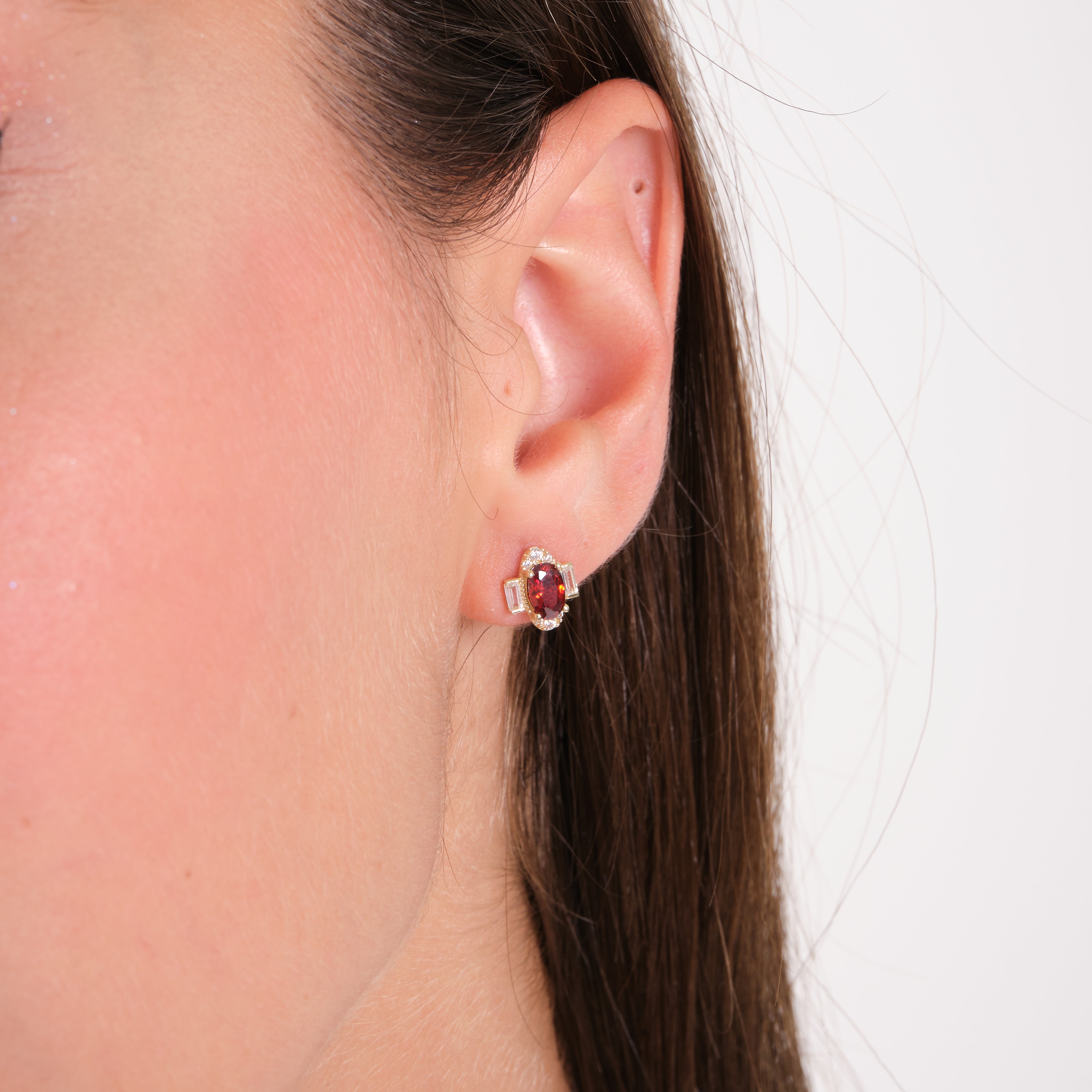 Close-up of an ear wearing a red gemstone earring with a white background
