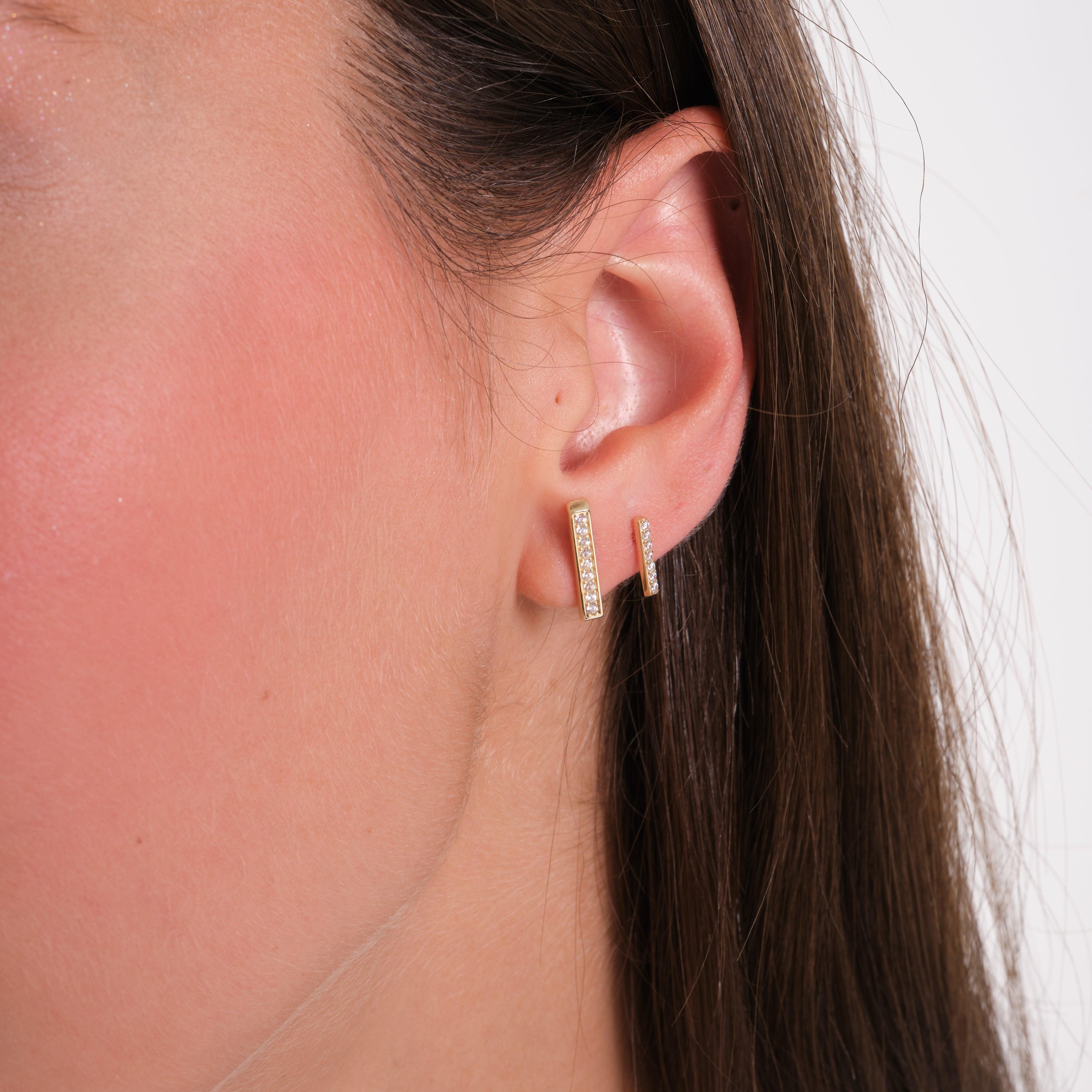Close-up of woman's ear wearing gold bar stud earrings with small diamonds